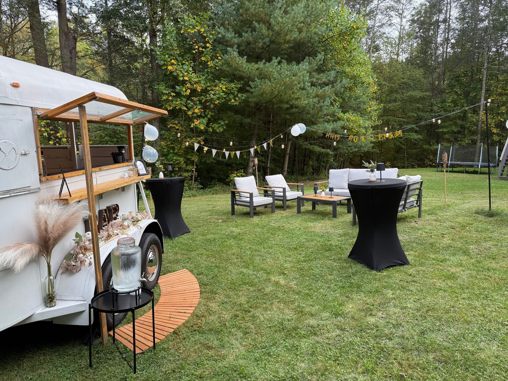 Horse trailer bar decorated for an outdoor event with seating, greenery, and string lights.