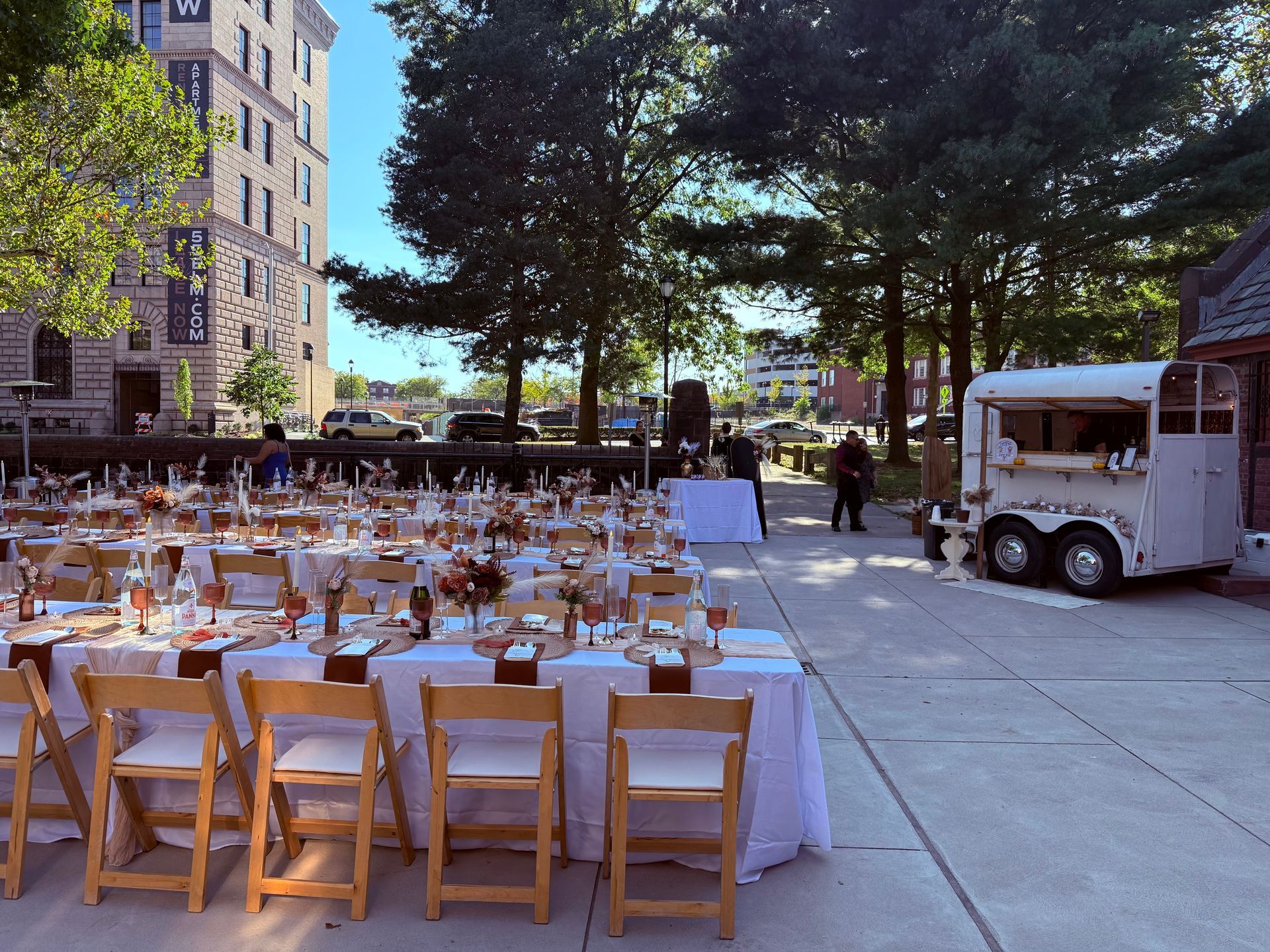 Outdoor reception with tables set for guests, white bar trailer.