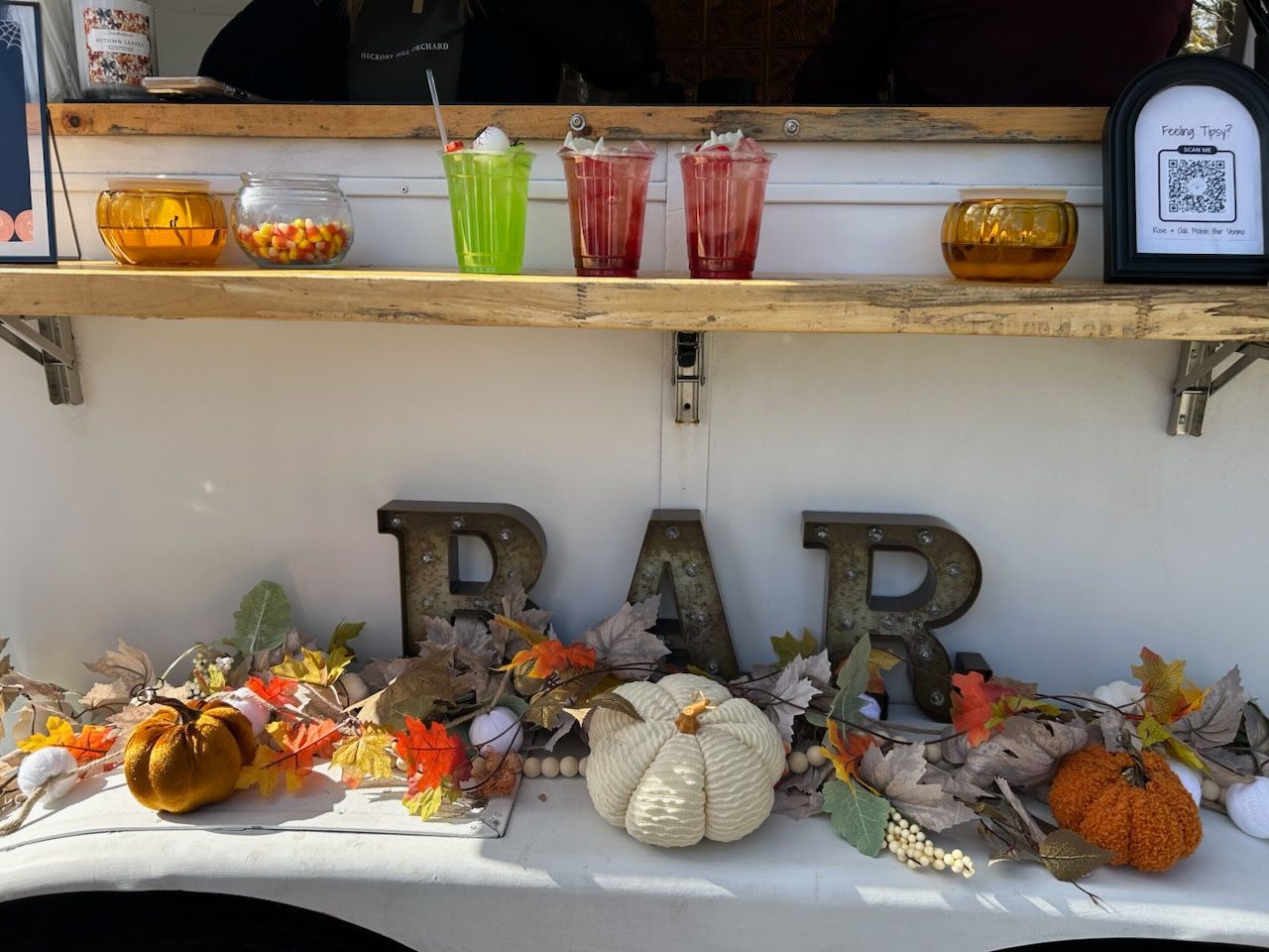 Bar decorated for fall with drinks, pumpkins, leaves, and “BAR” sign.