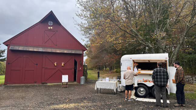 Red barn and horse trailer converted to a bar with patrons ordering drinks outside.