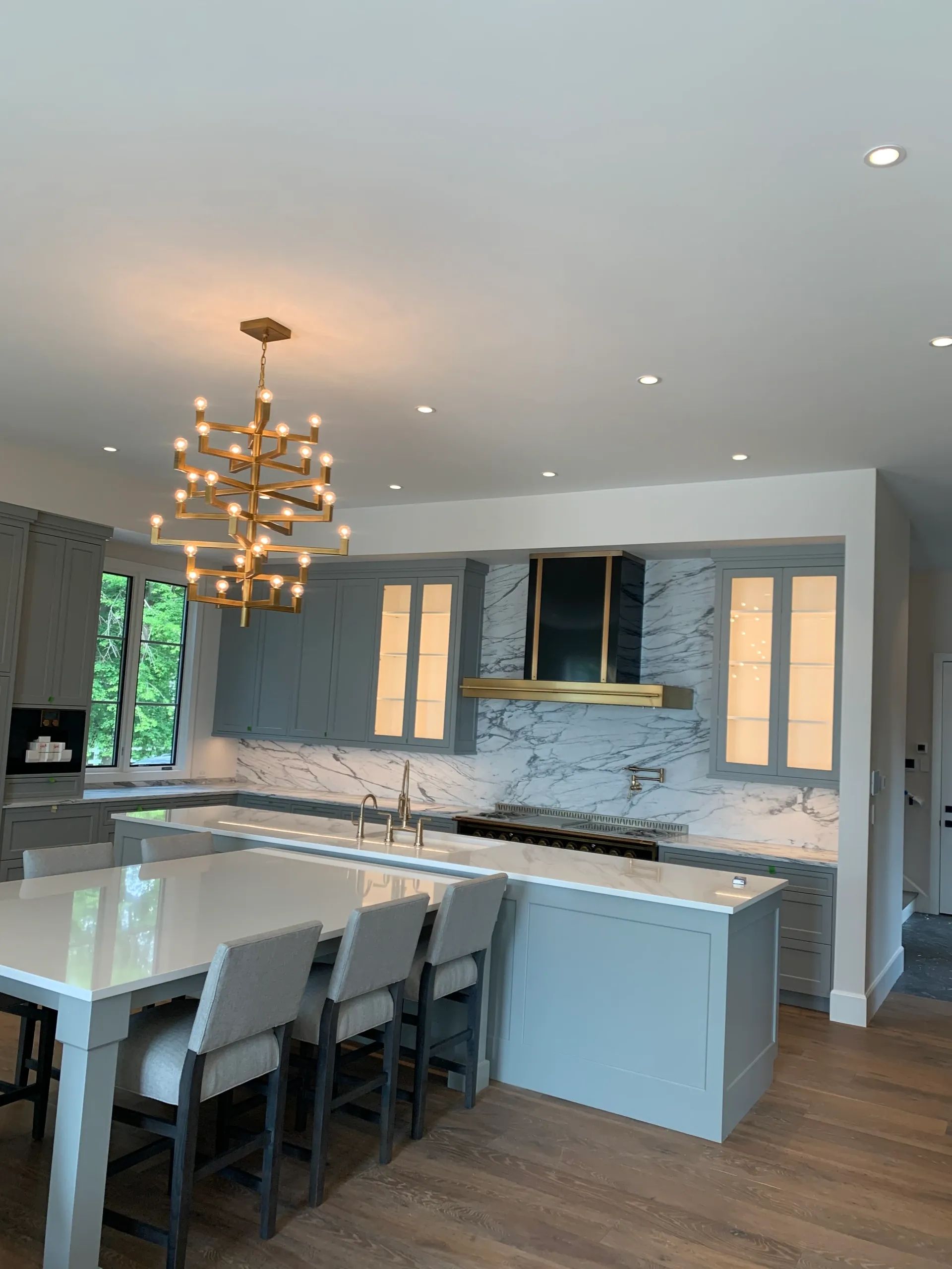 Modern kitchen with blue cabinets, marble counters, gold chandelier, and island with seating.