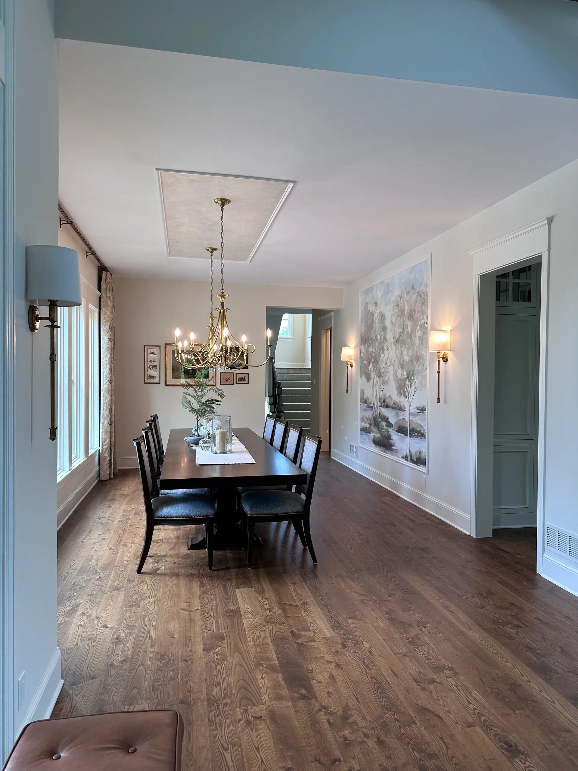 Formal dining room with dark wood table, chairs, and floors; chandelier; mural; and arched doorway.