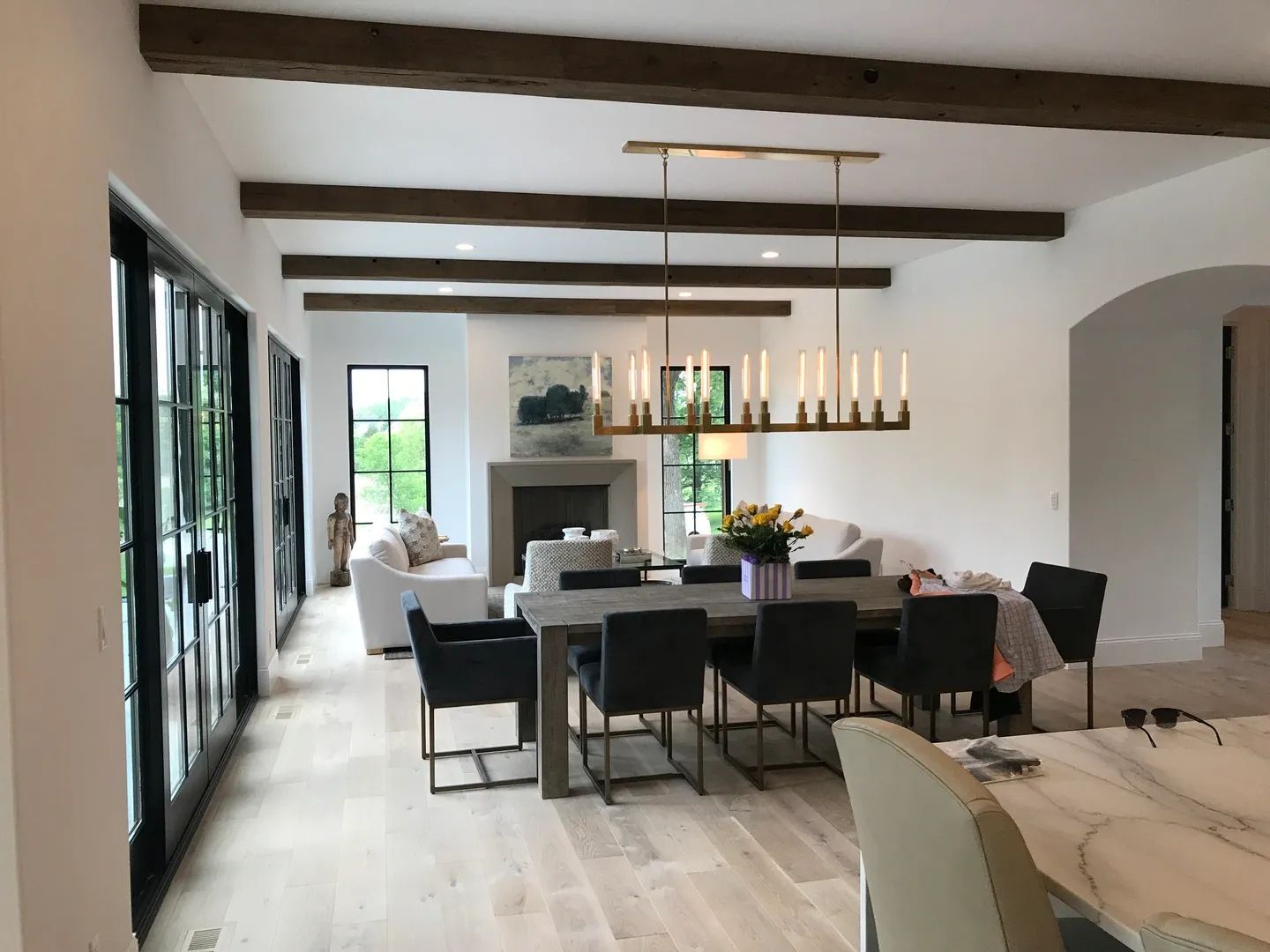 Dining room with wooden beams, a long table with chairs, and a fireplace. Light wood floors.