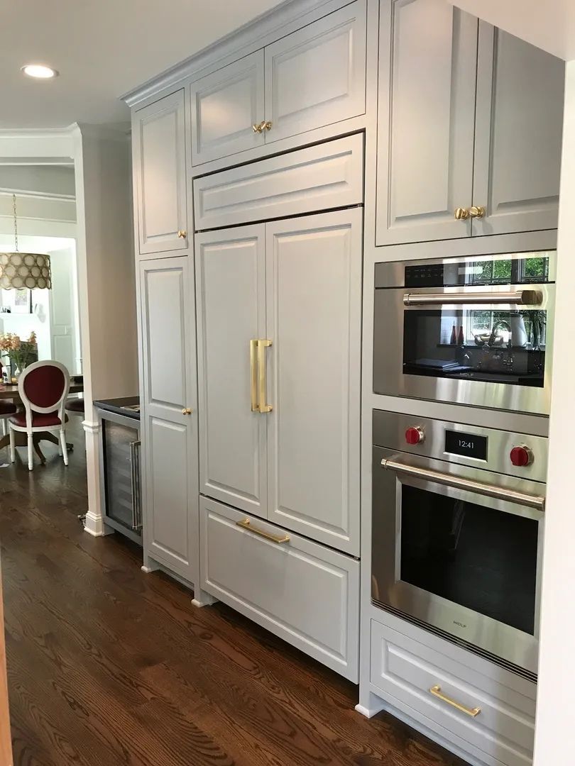 Light blue kitchen cabinets with gold hardware, built-in refrigerator, microwave, and oven, on a dark wood floor.