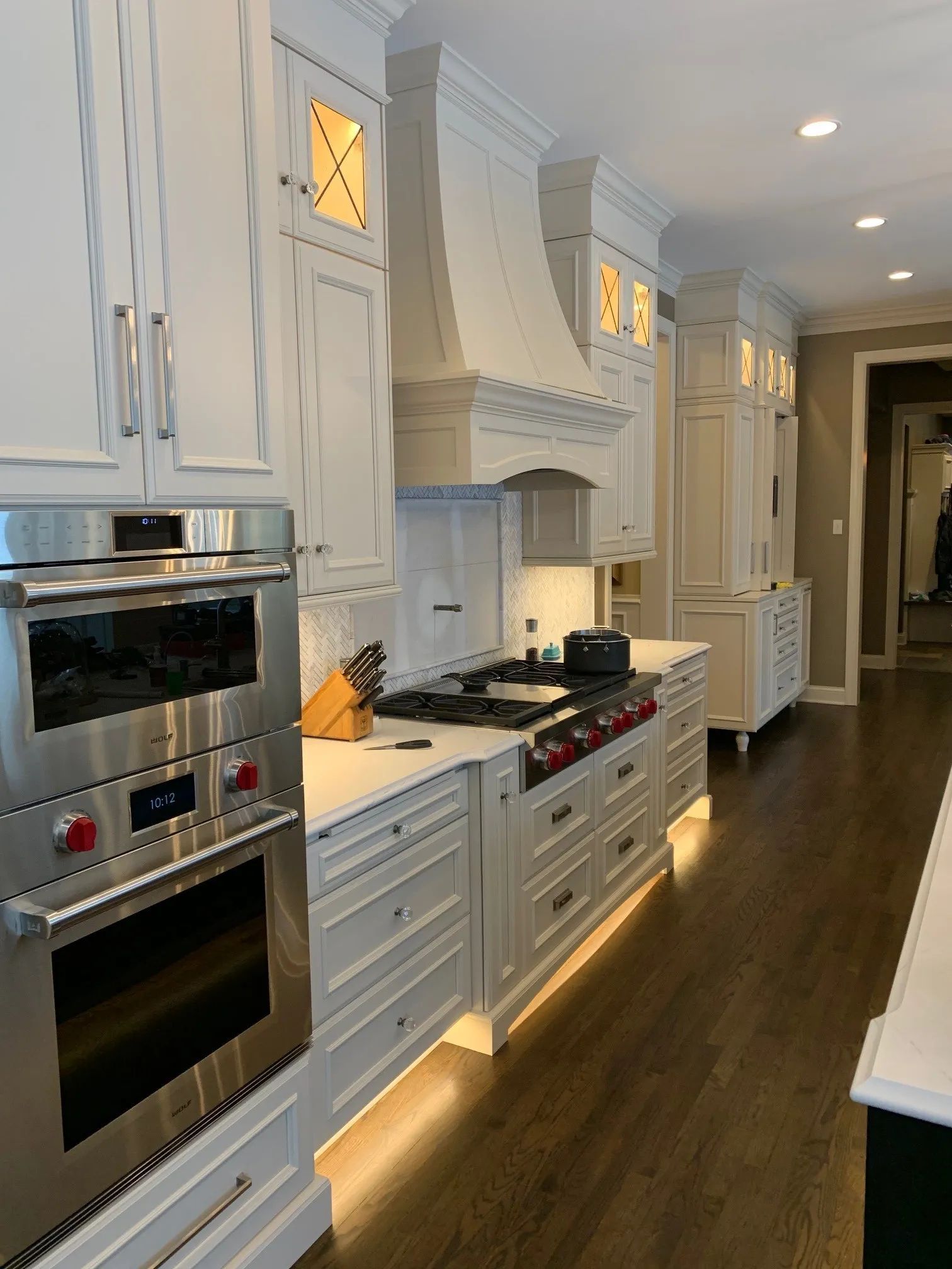 White kitchen with stainless steel appliances, stove with hood, and under-cabinet lighting.