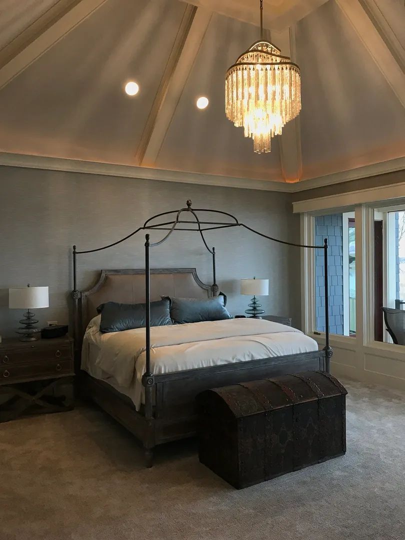 Bedroom with canopy bed, chandelier, nightstands, and chest at the foot of the bed.
