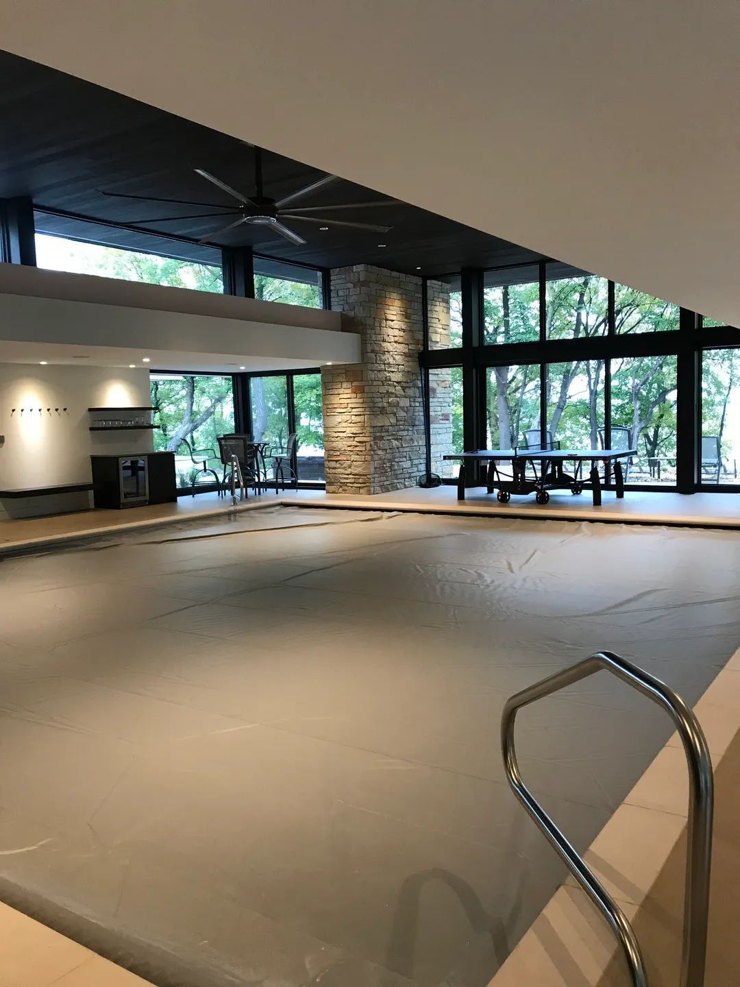 Indoor swimming pool with closed cover, surrounded by large windows and a stone accent wall.