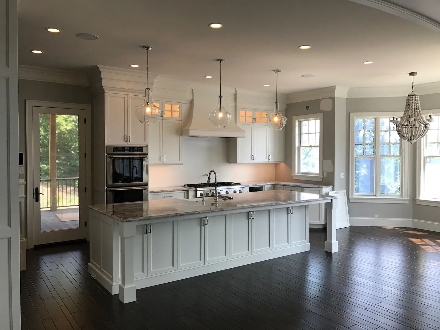 Elegant white kitchen with island, stainless steel appliances, and dark hardwood floor.