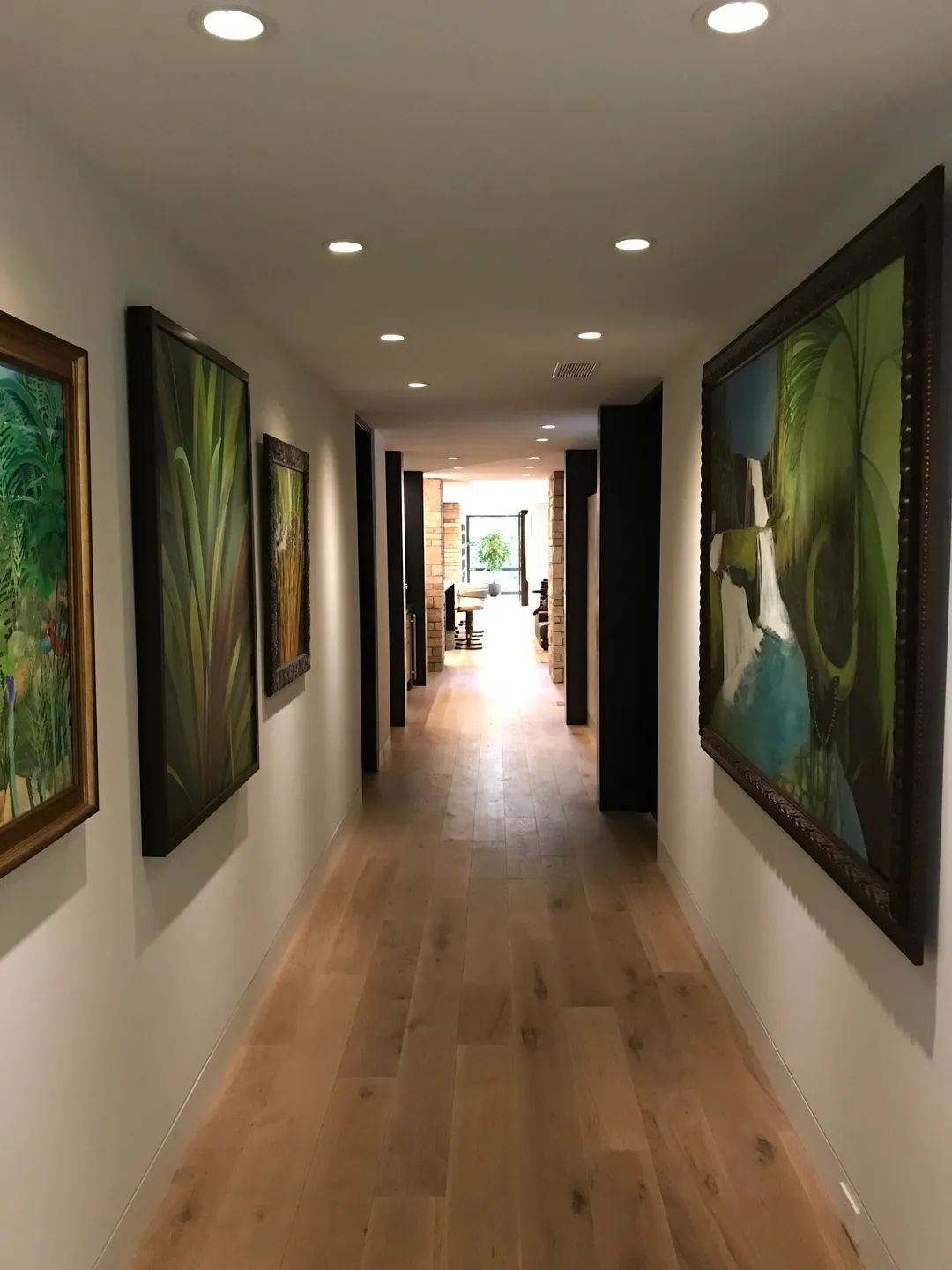 Hallway with light wood floor and white walls, decorated with framed paintings.