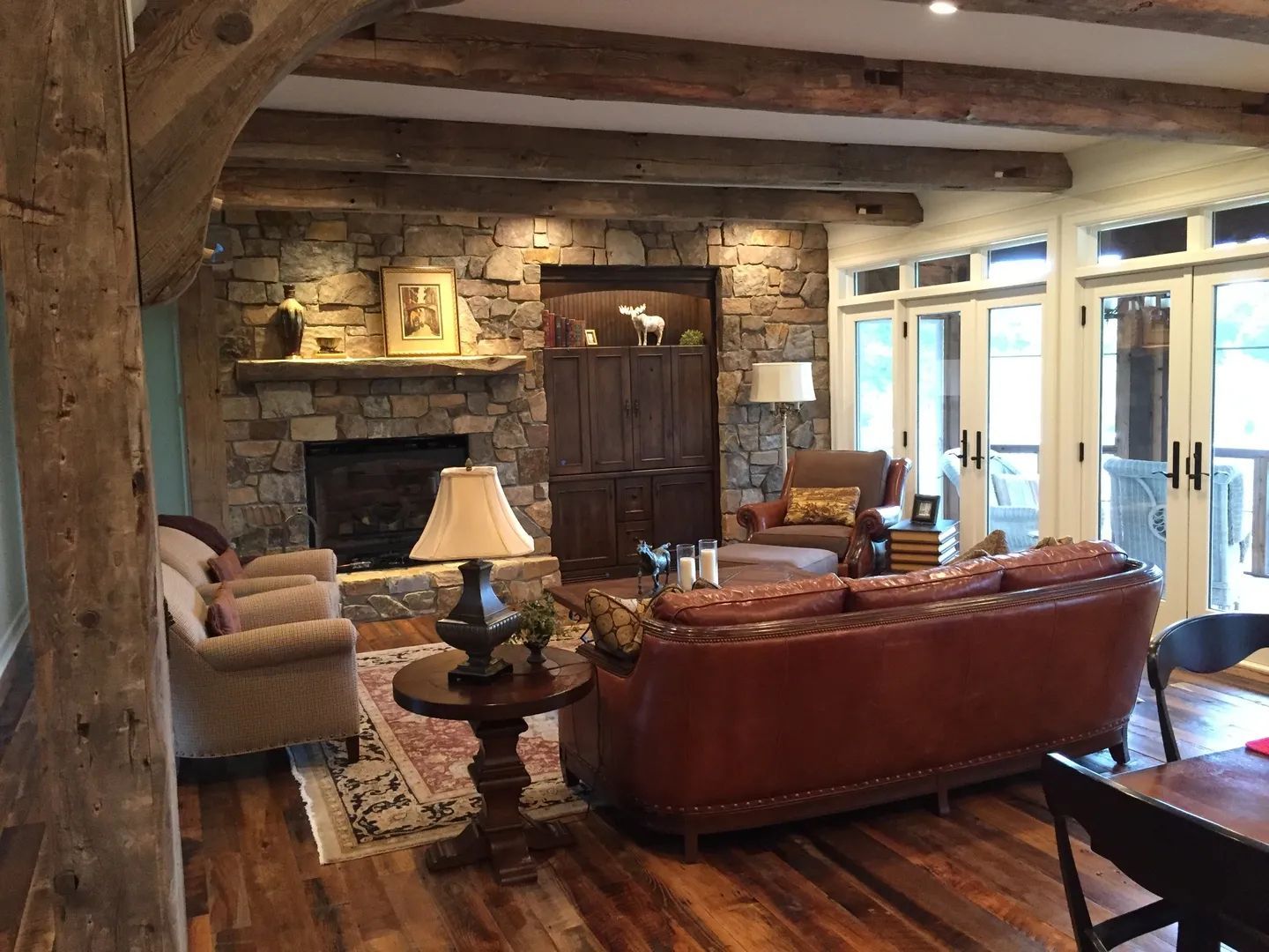 Cozy living room with stone fireplace, wooden beams, leather sofa, and large windows.
