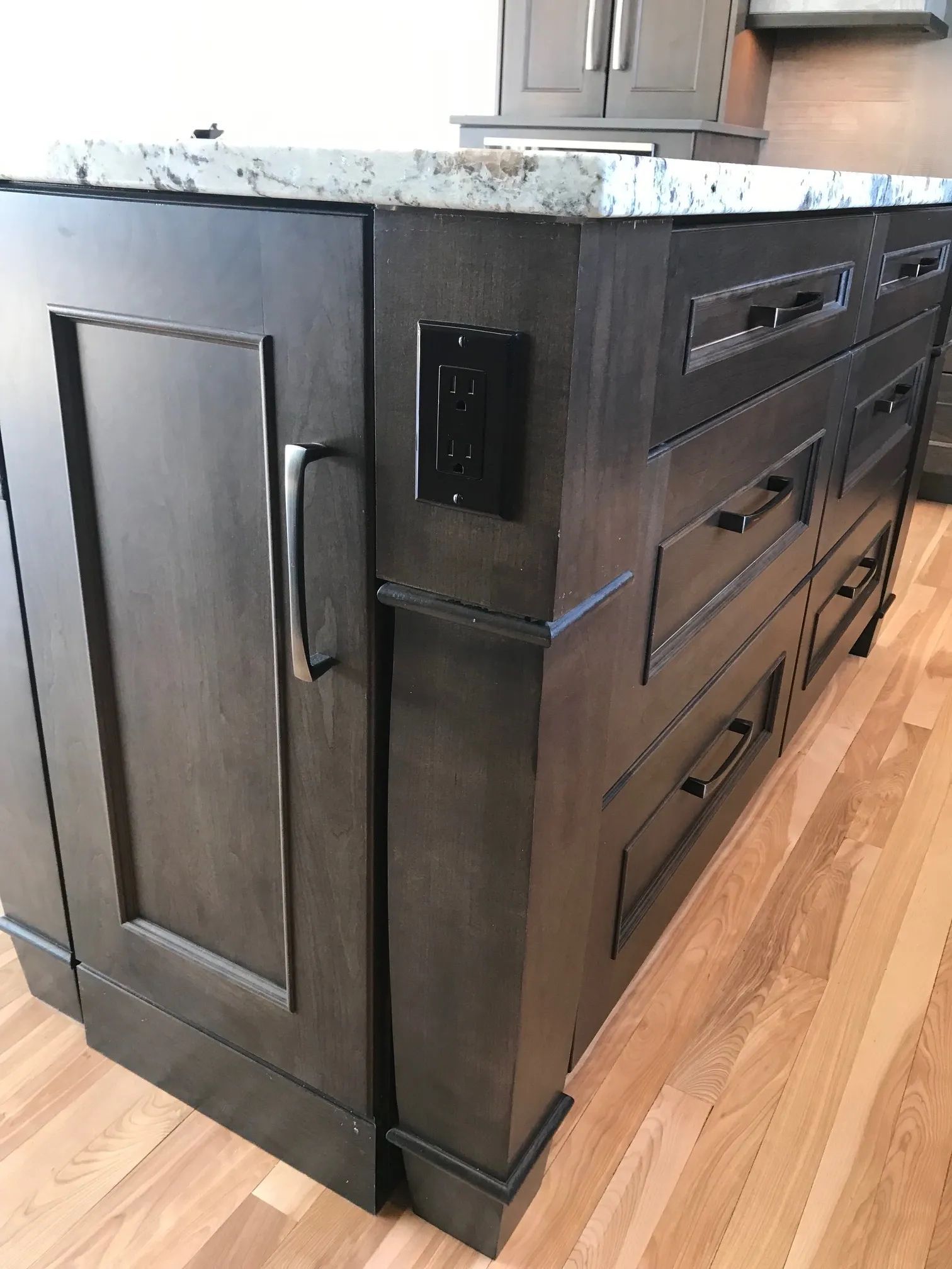 Dark wood kitchen island with drawers, outlet, and countertop, situated on hardwood floor.