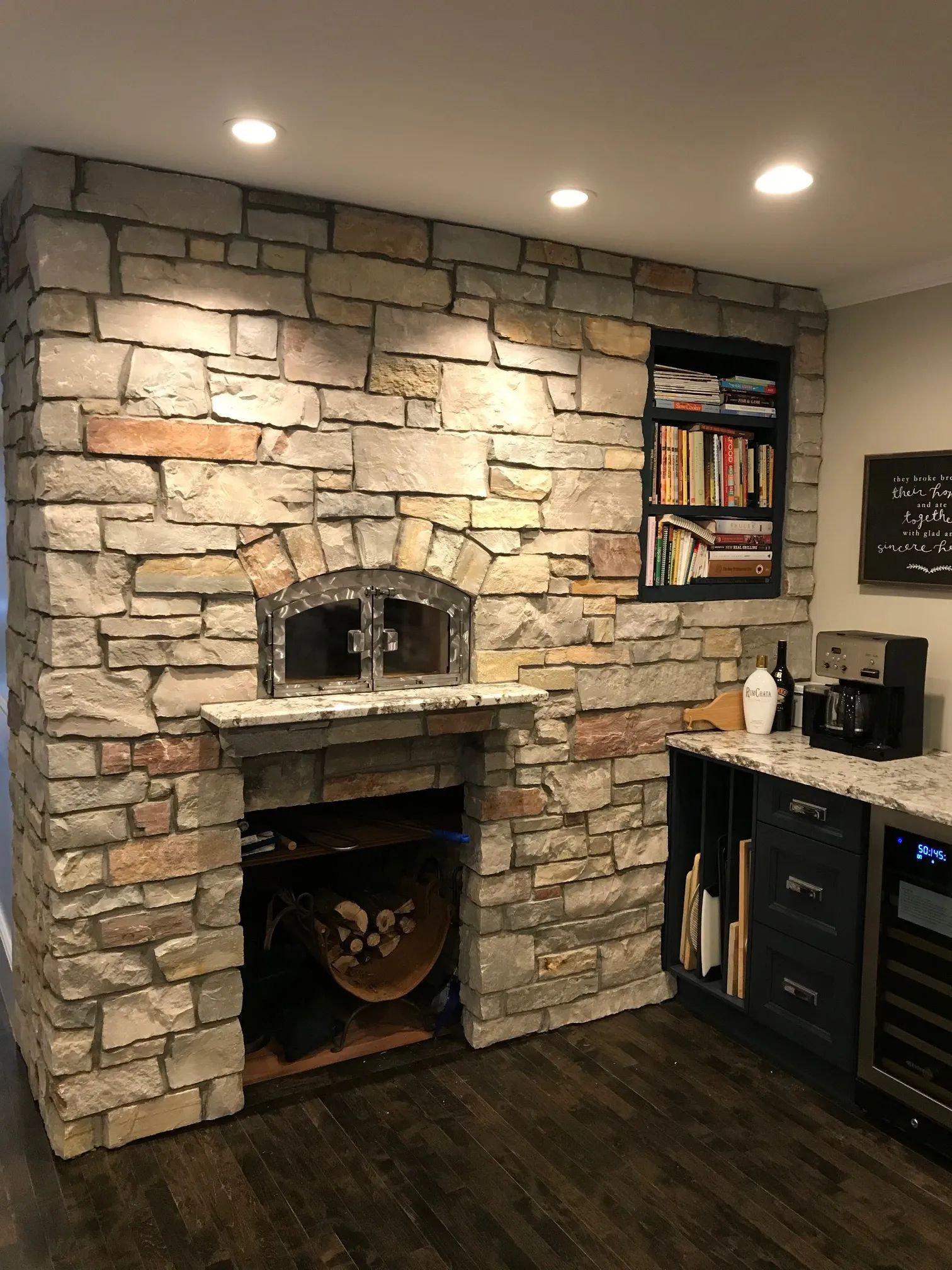 Stone pizza oven built into a wall with a niche bookcase, dark cabinetry, and wood flooring.