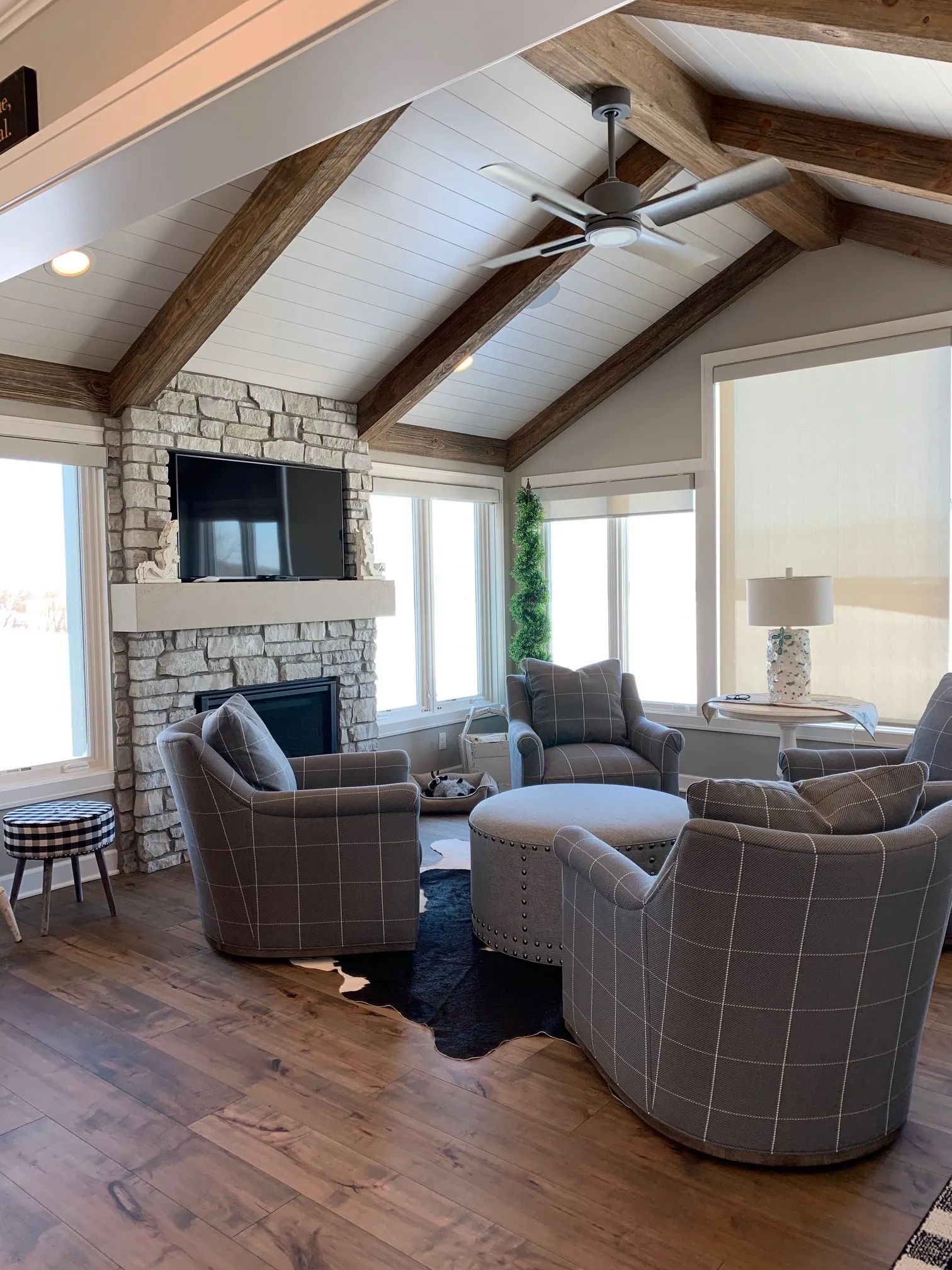 Living room with stone fireplace, wood beams, gray patterned chairs, and a cowhide rug.