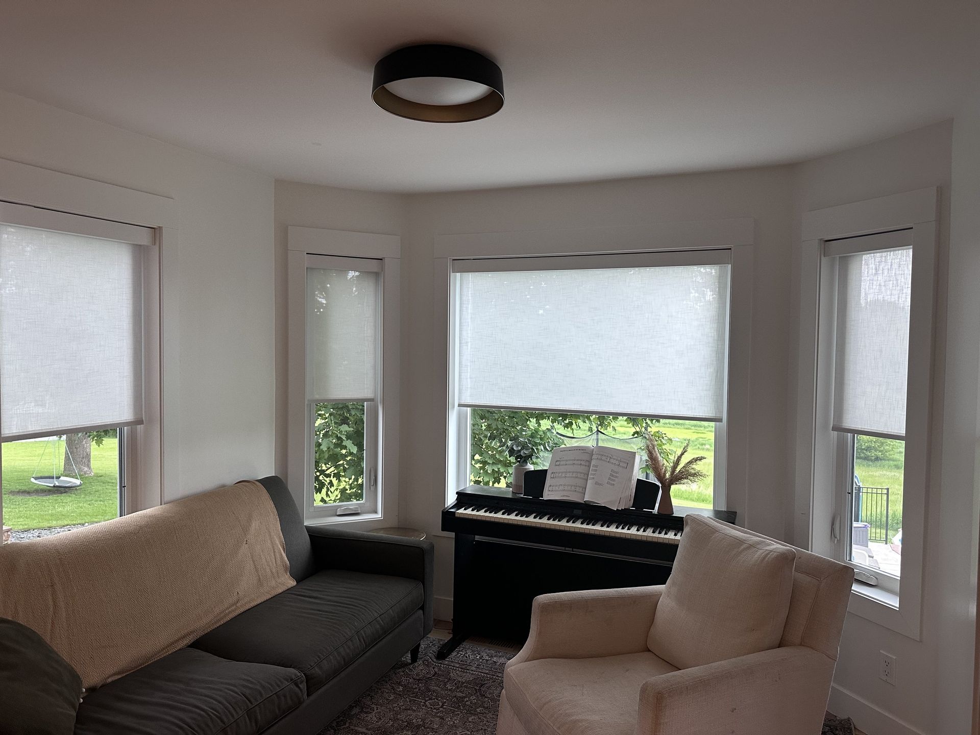 A living room with a couch, armchair, piano, and windows with shades.