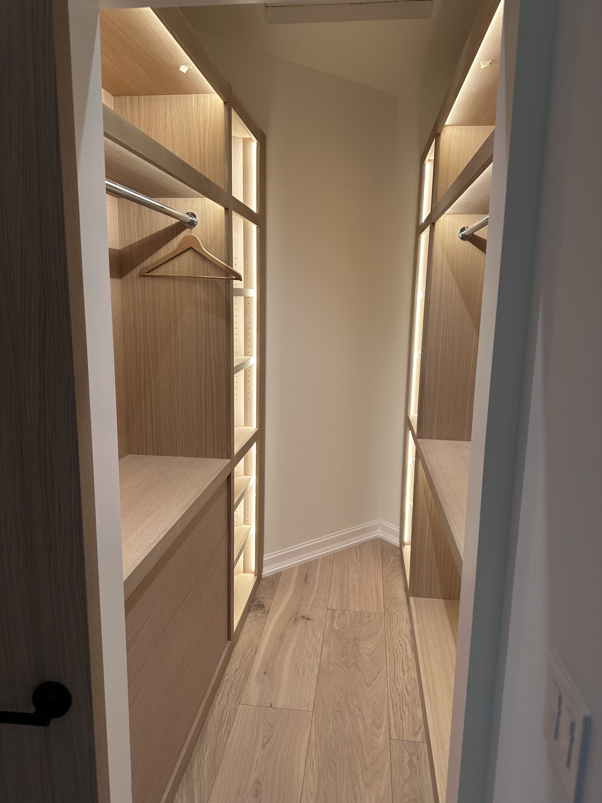 Walk-in closet with wood shelves, lit with warm lights. Empty with wood-look floor.