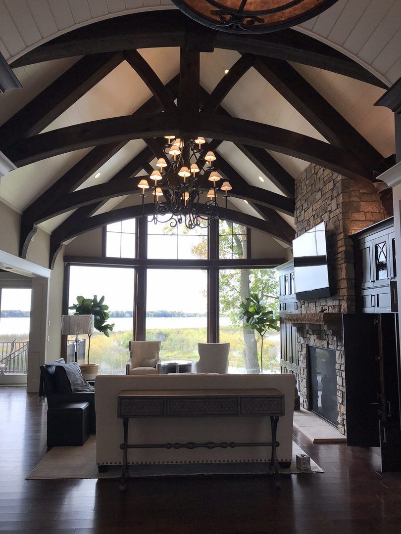 Living room with dark beams, large windows overlooking water, and a chandelier.