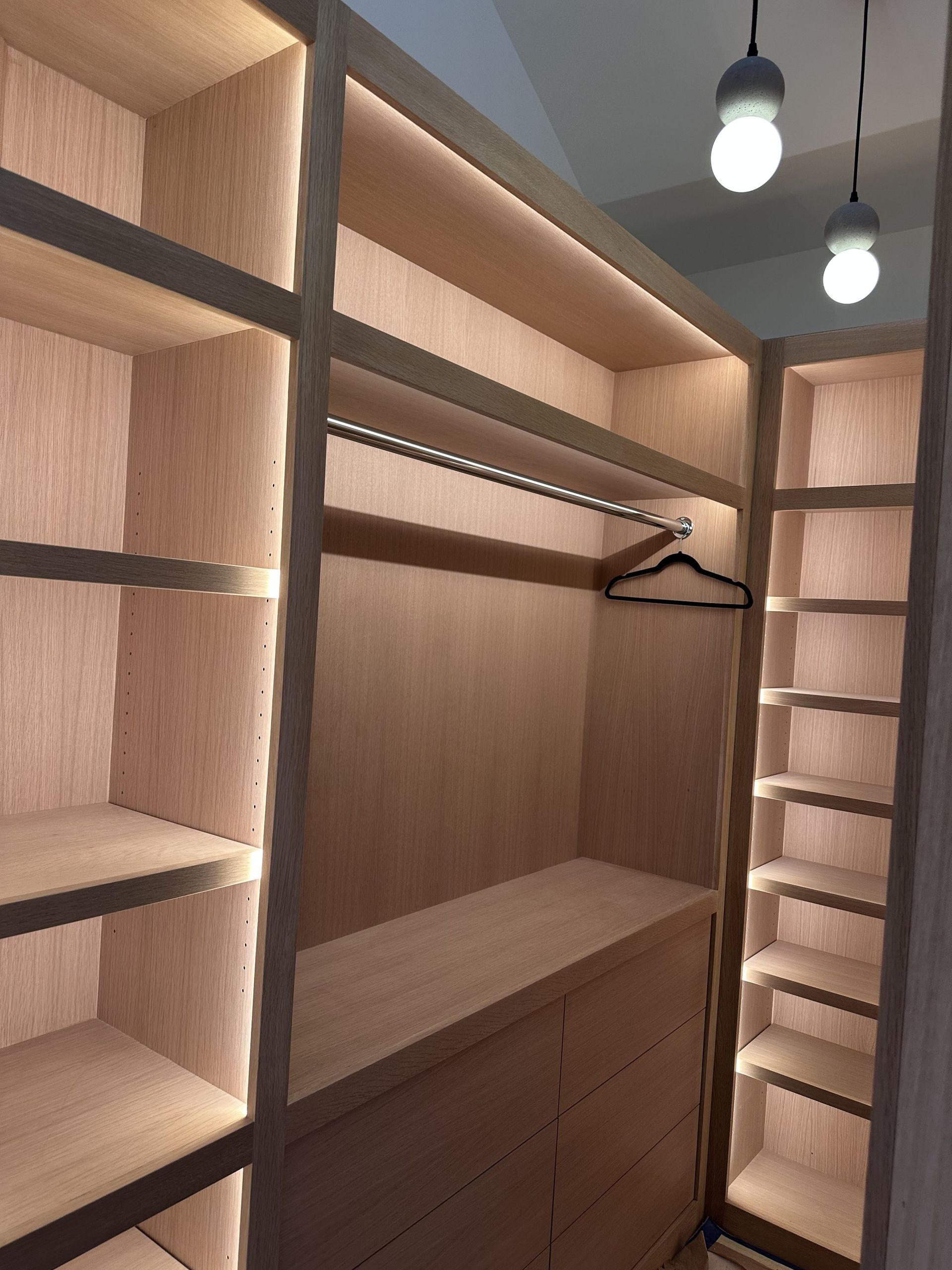 Wooden walk-in closet with shelves and drawers, lit by internal lights.