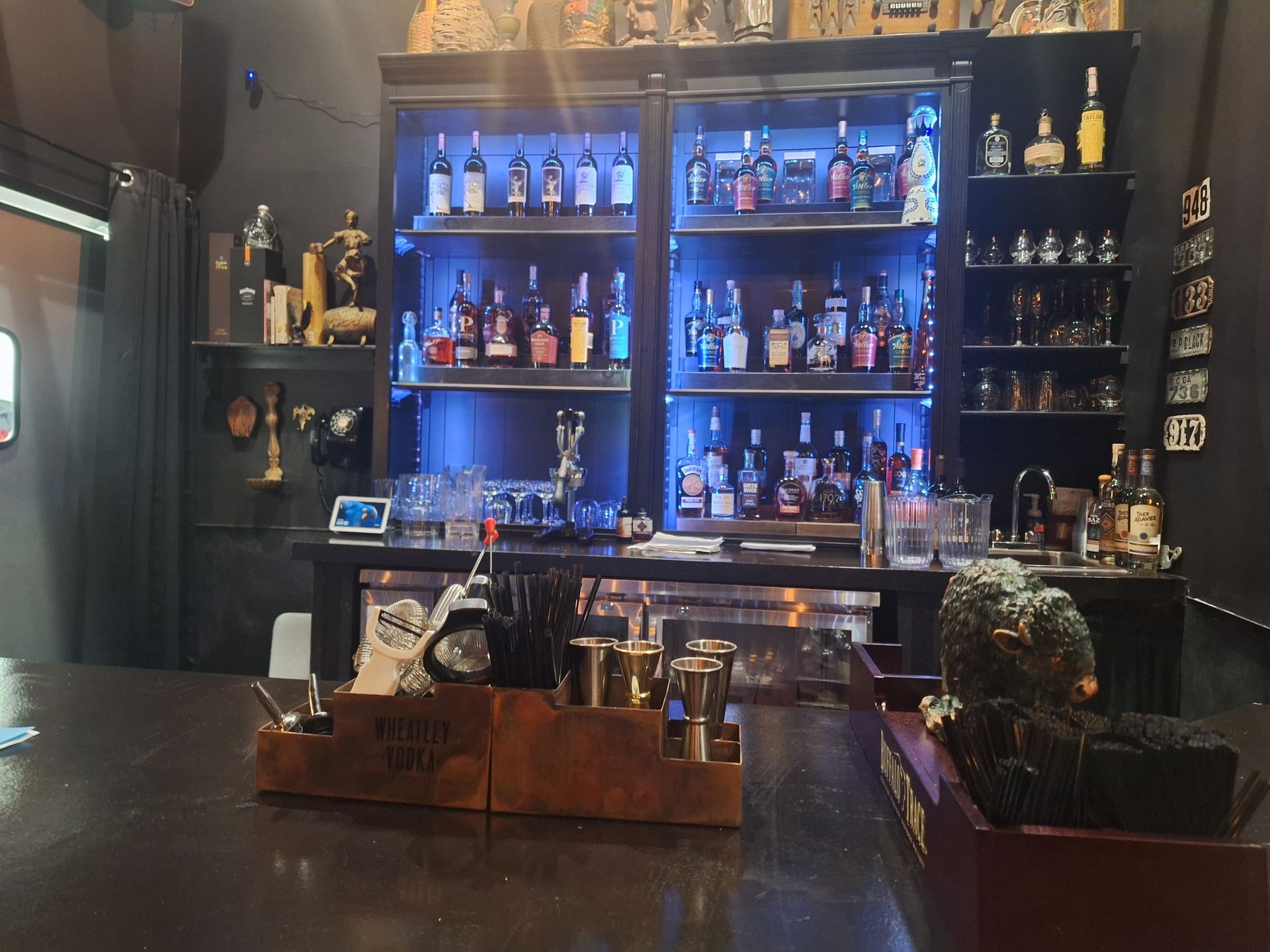 A bar with a dark countertop and shelves filled with liquor bottles, backlit with blue light.