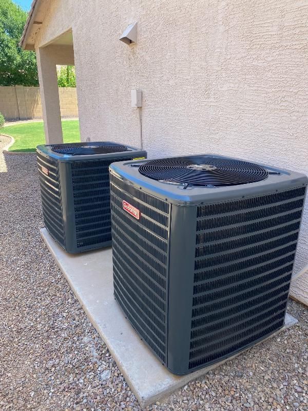 Two air conditioners are sitting next to each other on the side of a house.