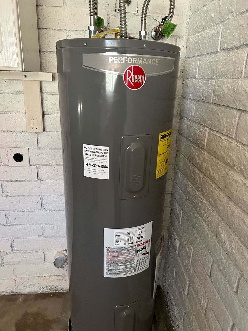 A gray water heater is sitting next to a white brick wall.