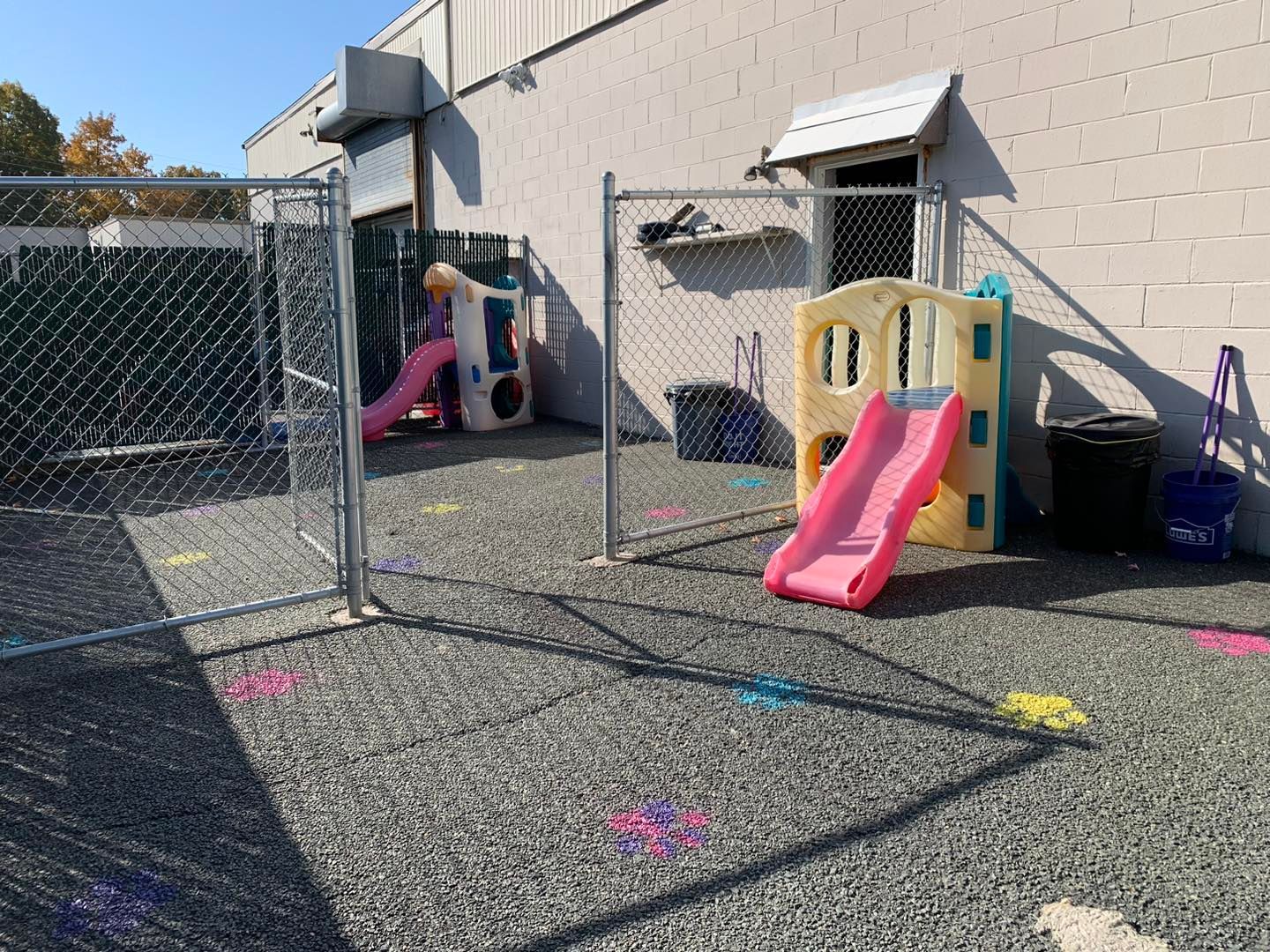 A child is playing in a playground with a slide and swings behind a chain link fence.