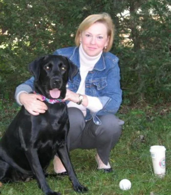 A woman is kneeling down next to a black dog