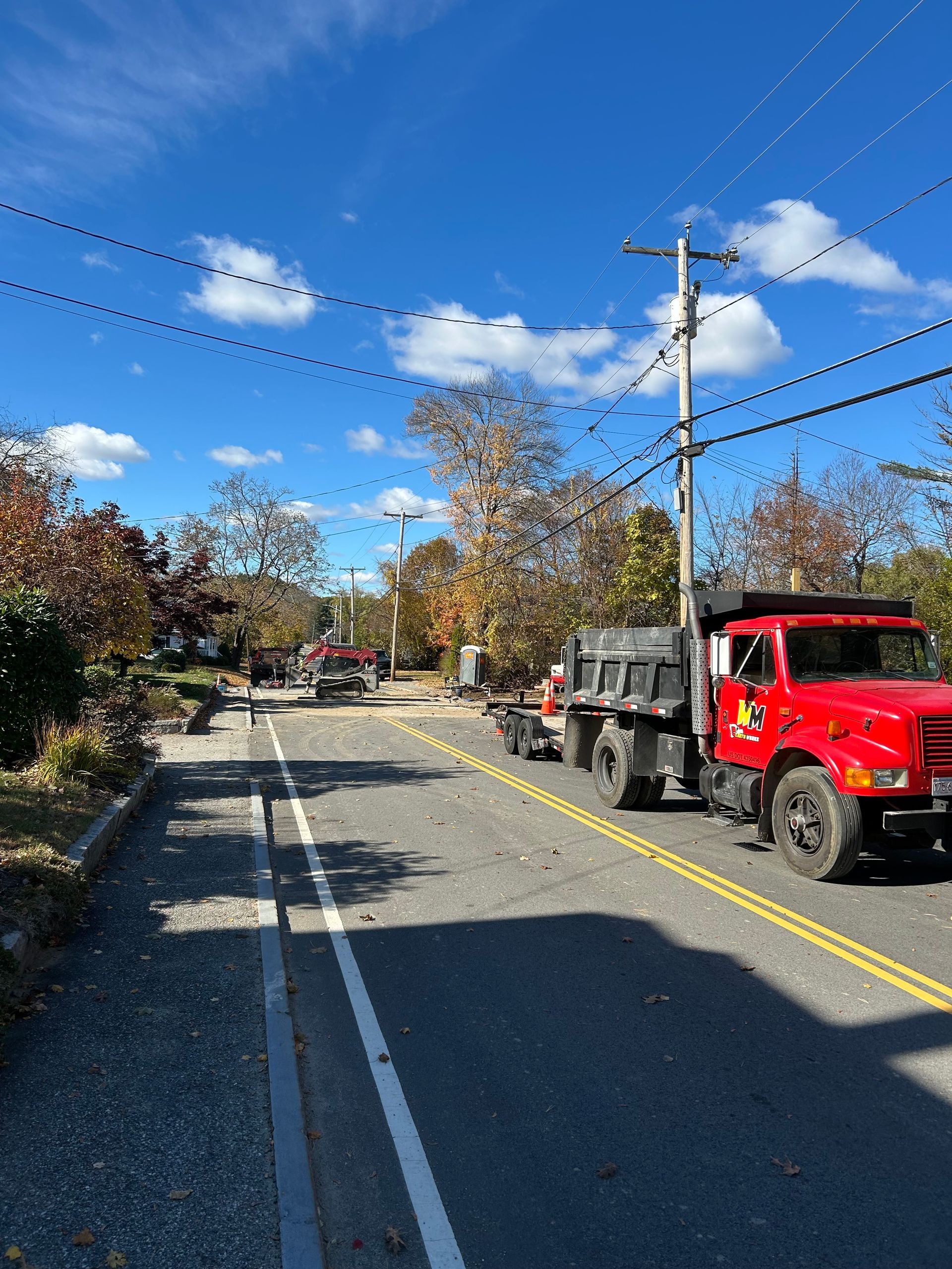 Red utility truck parked on a sunny street with autumn trees and power lines overhead