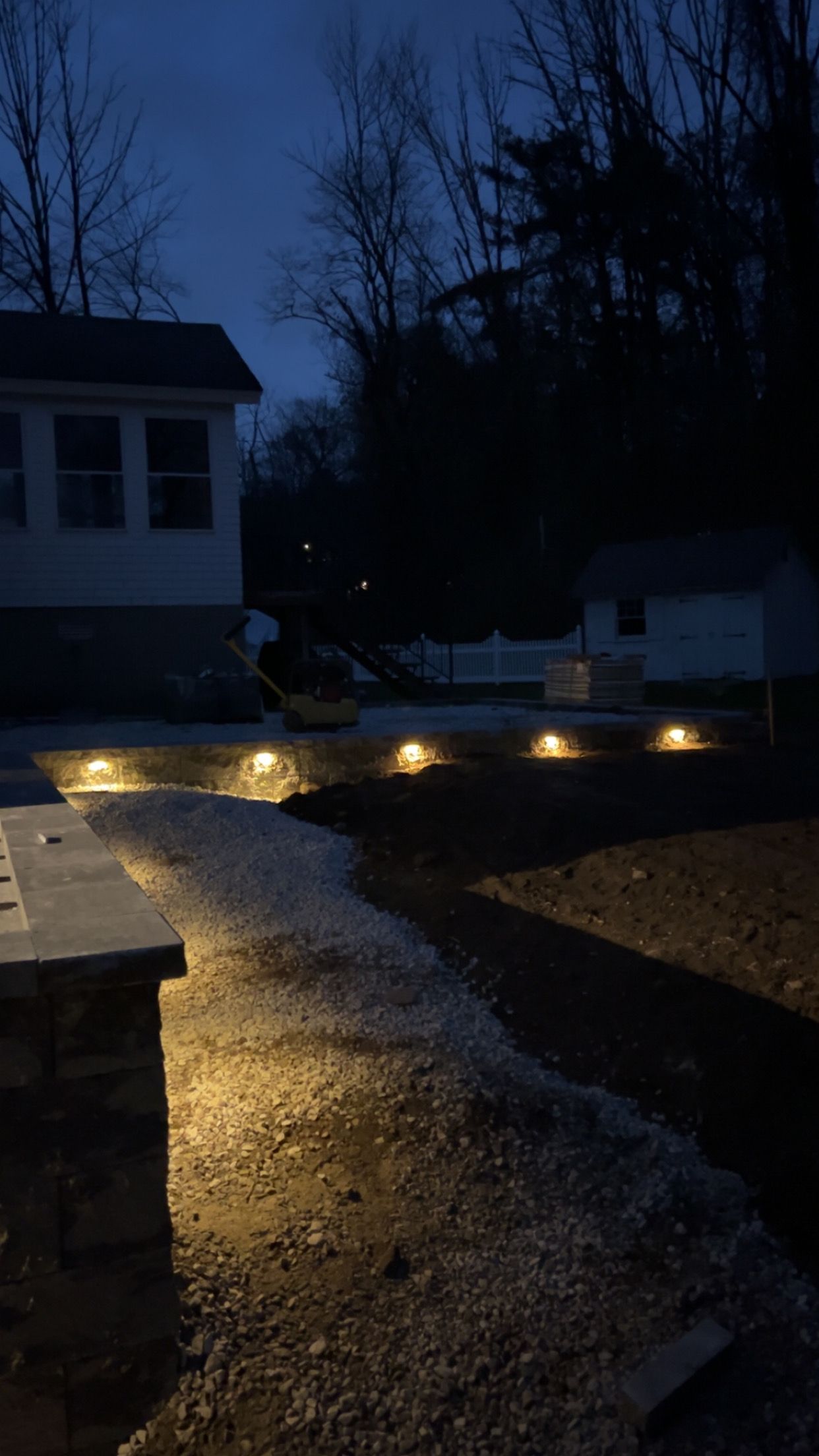 Dimly lit front walkway with warm ground lights leading to a house at dusk.
