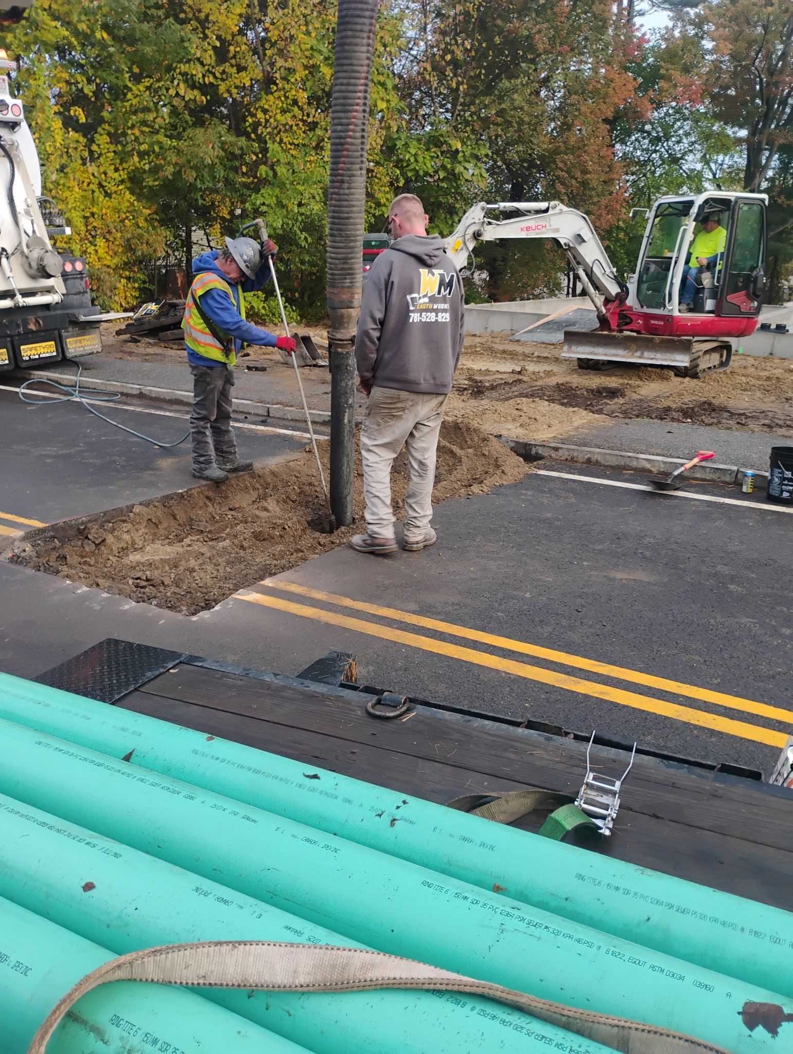 Roadwork crew digging a trench beside a street with pipes in the foreground.