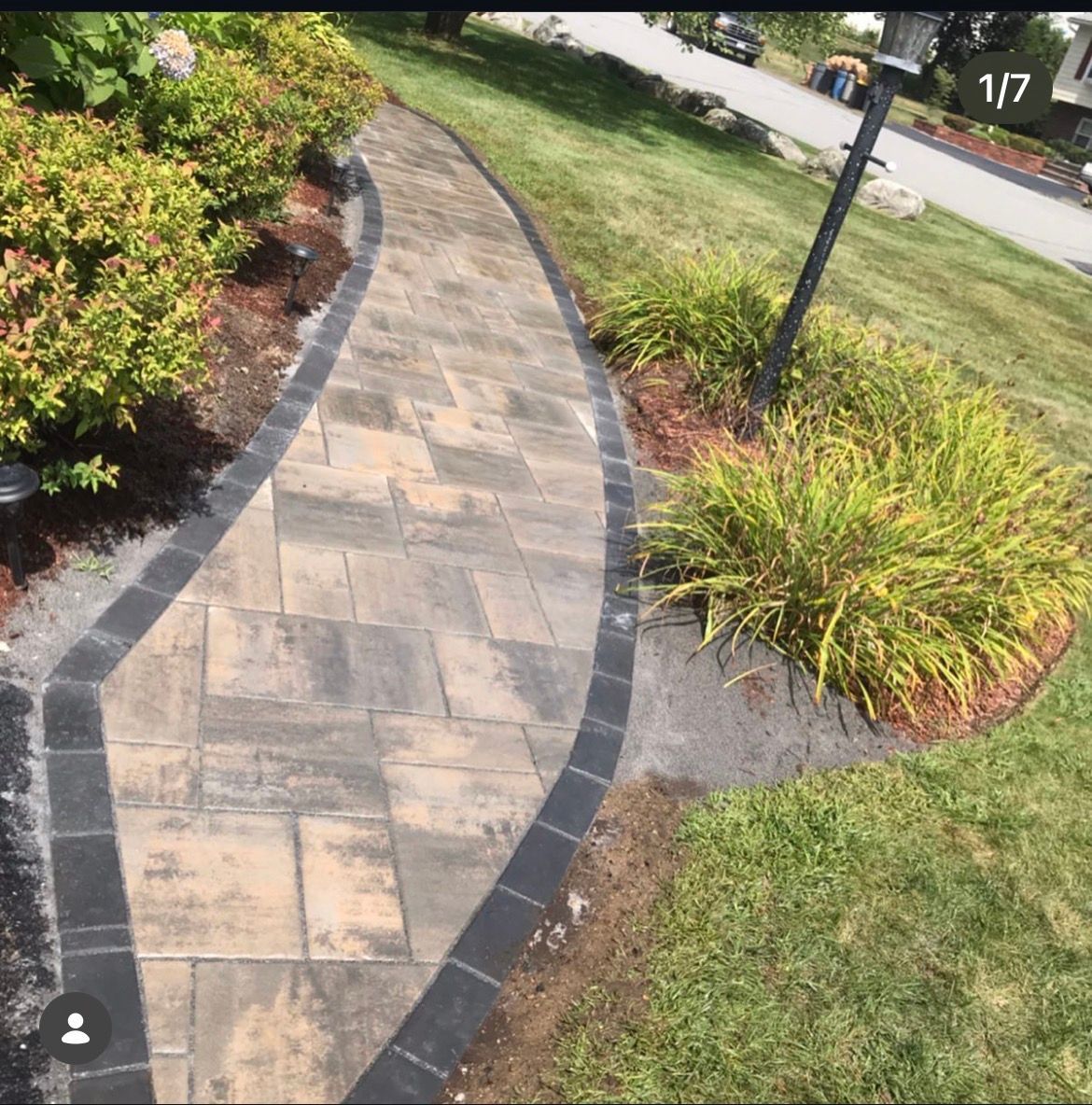 Curved stone walkway bordered by mulch, shrubs, and grass in a landscaped yard