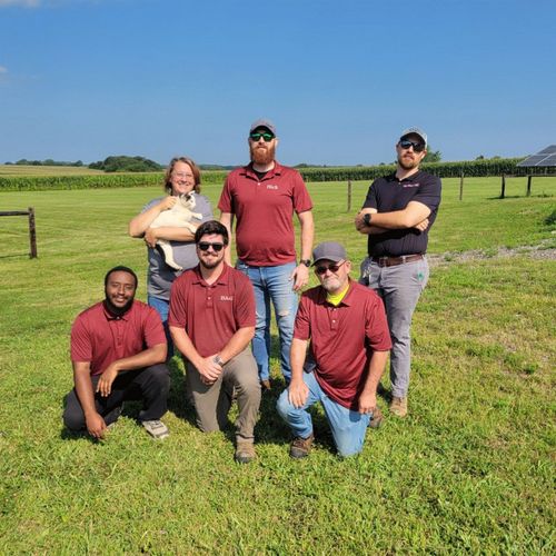 Six people posing in a grassy field under a clear blue sky, wearing red shirts.