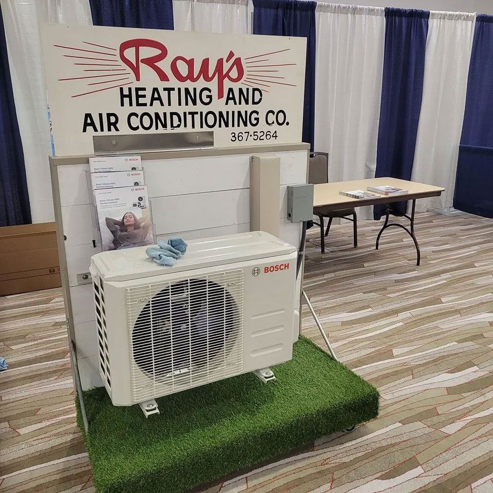 HVAC display booth with outdoor AC unit on artificial grass and Raabe’s Heating and Air Conditioning sign