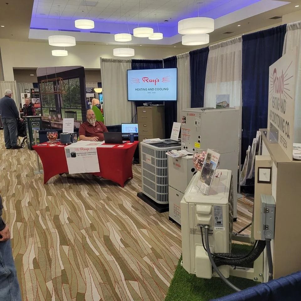 Vendor booth at an indoor expo with red tablecloths, display screens, and a carpeted walkway under blue-lit ceiling lights