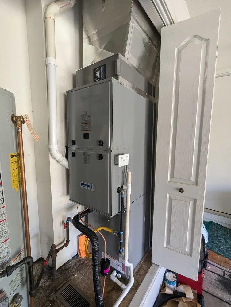 Gray HVAC furnace and utility equipment in a narrow closet beside a white door.