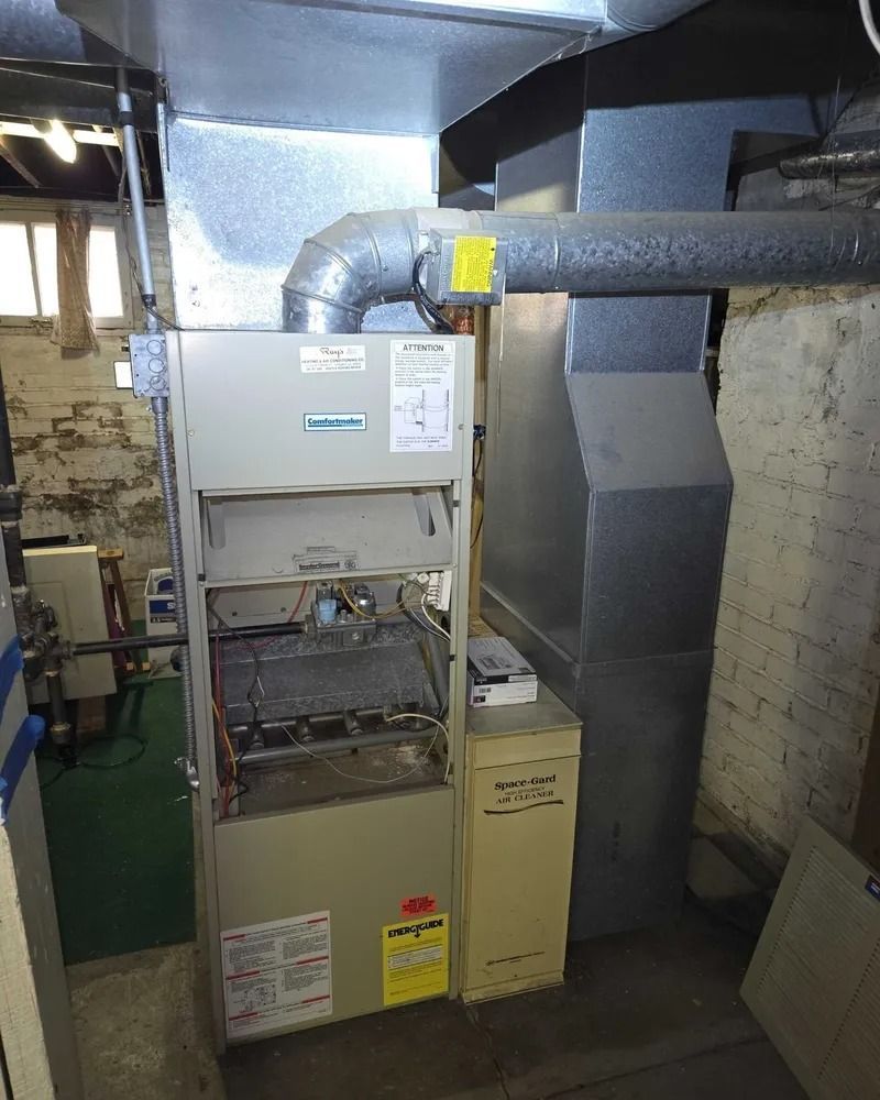 Basement HVAC furnace with ductwork and utility equipment against a concrete wall.