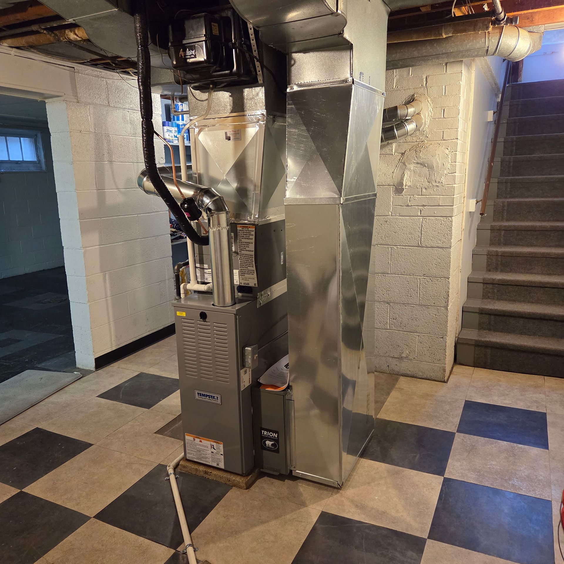 Basement utility room with a large silver furnace and ductwork on a tiled floor