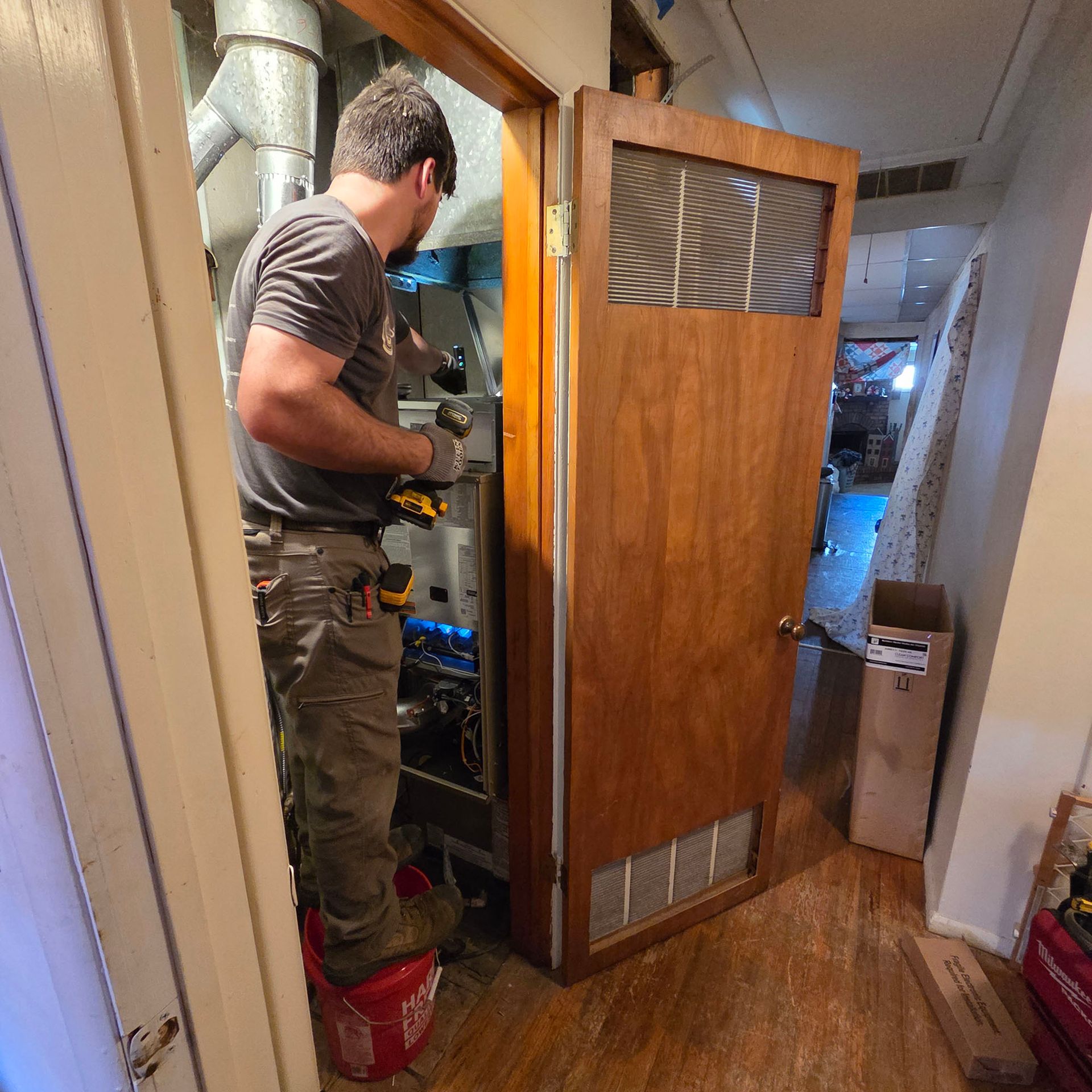 Technician servicing equipment inside a small hallway utility closet with the door open