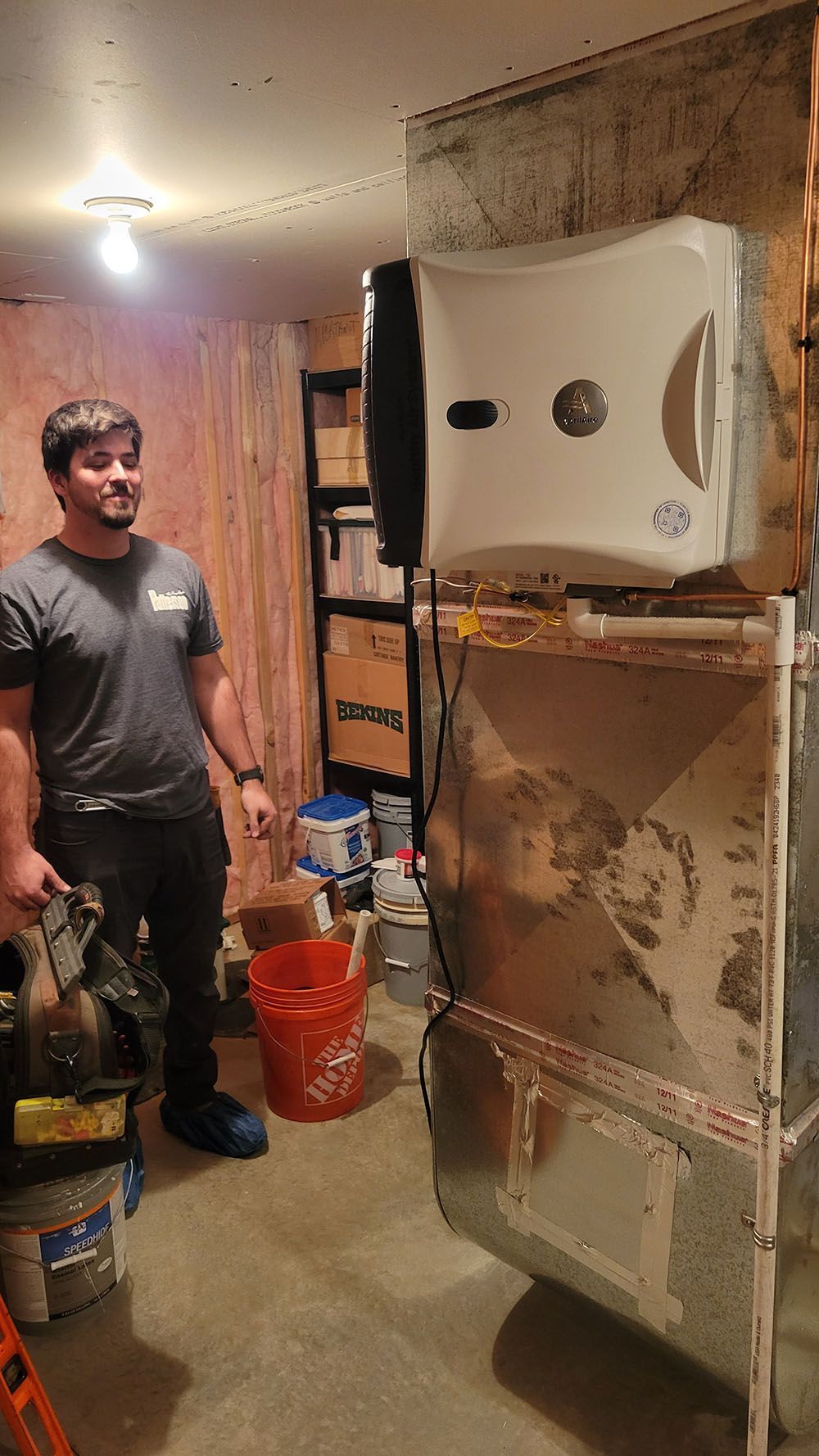 Person standing in a small room beside an open wall-mounted appliance with exposed insulation and tools nearby