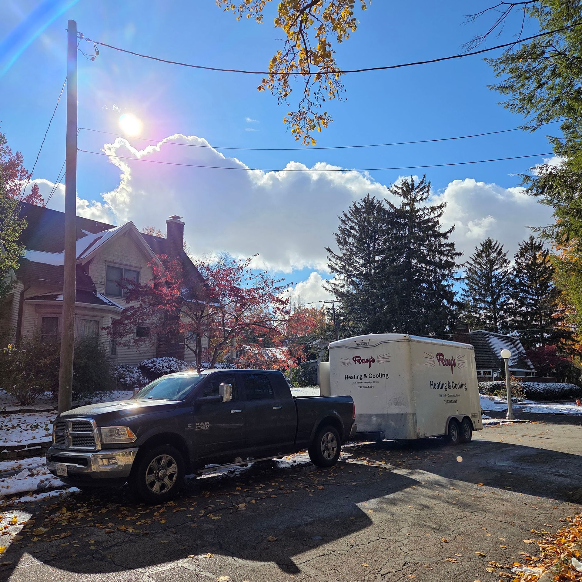 Pickup truck towing a white trailer on a sunny residential street with houses and autumn trees