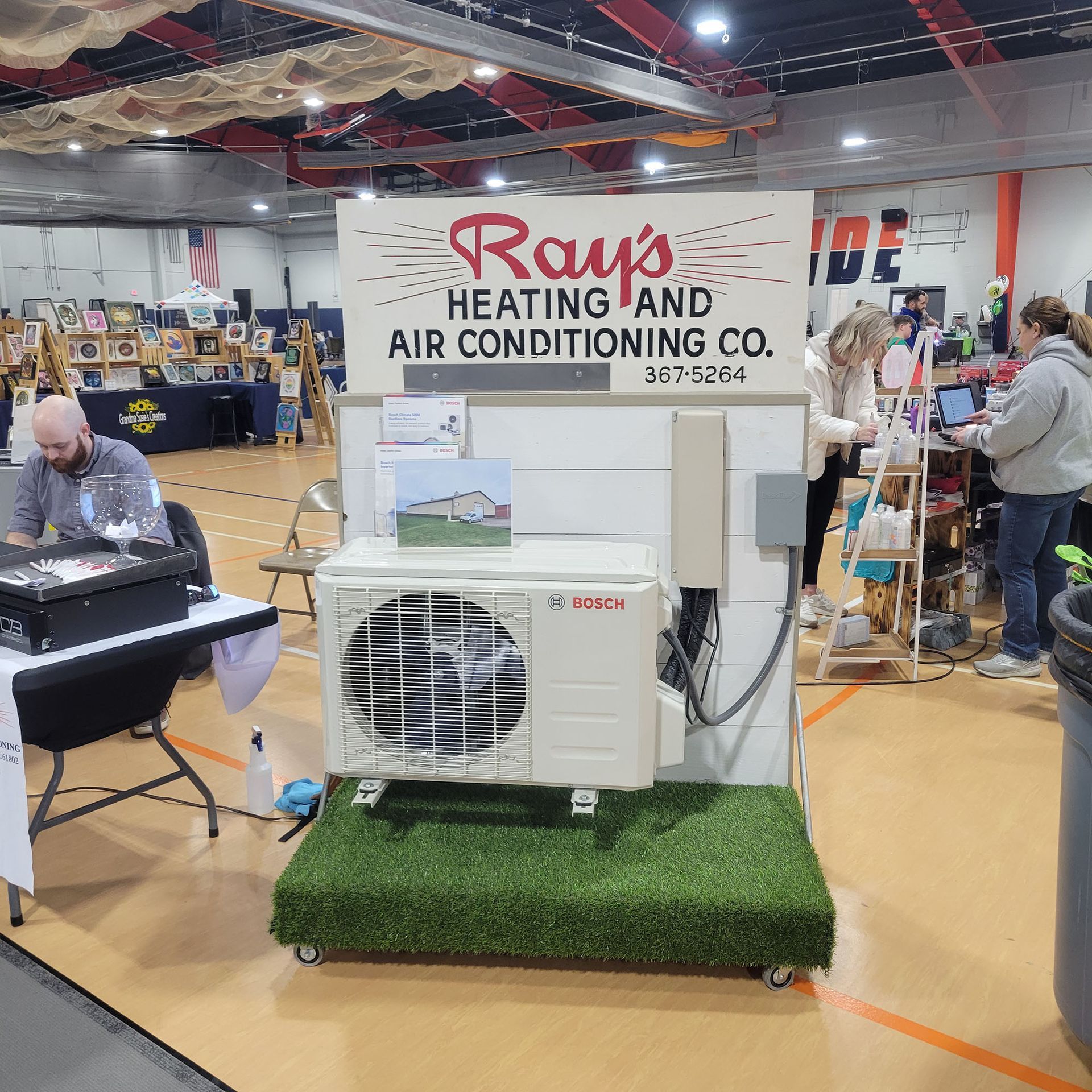 Trade show booth for Rays Heating and Air Conditioning Co. with HVAC unit display on artificial grass.