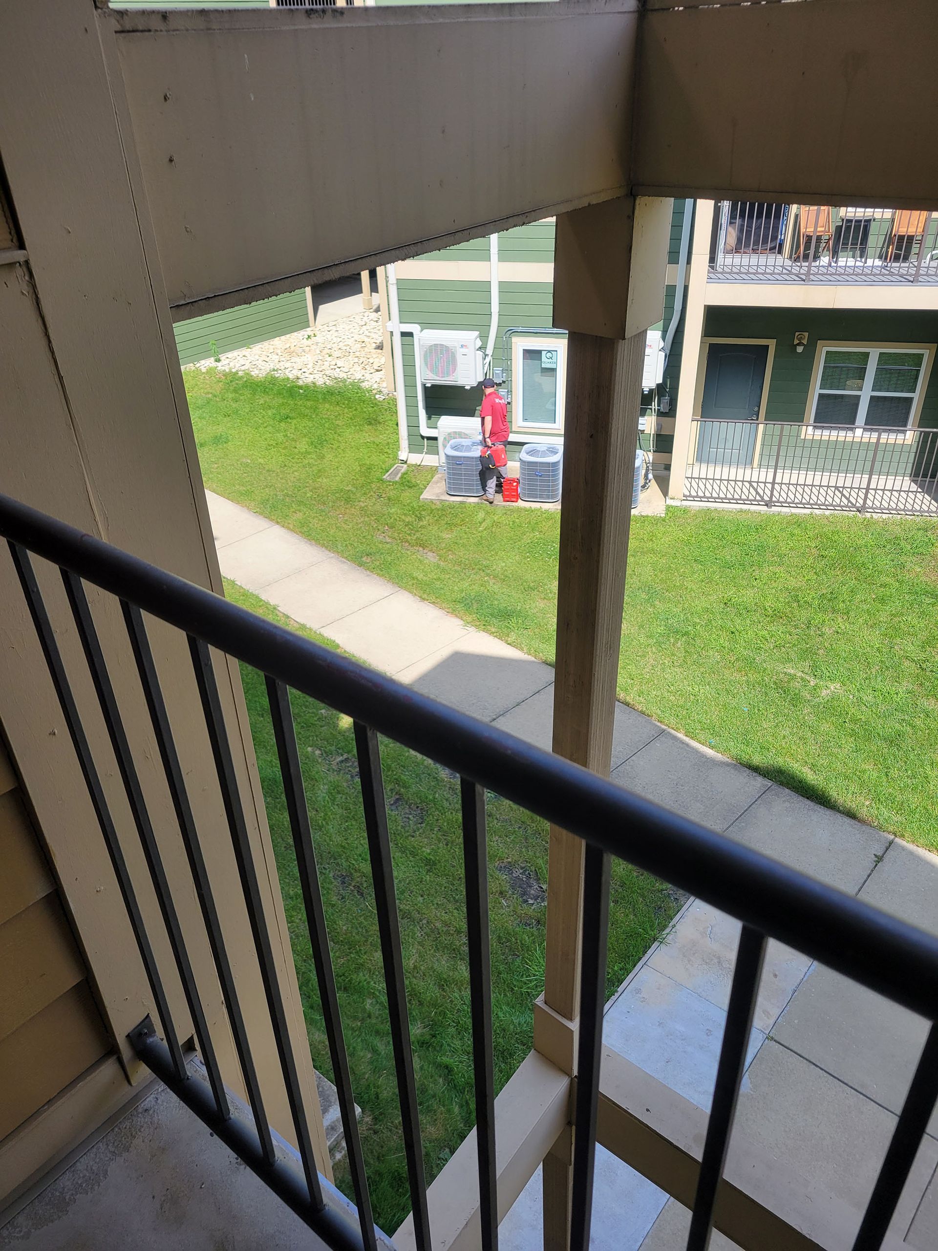 Apartment balcony railing overlooking a walkway and courtyard with a person near a green door