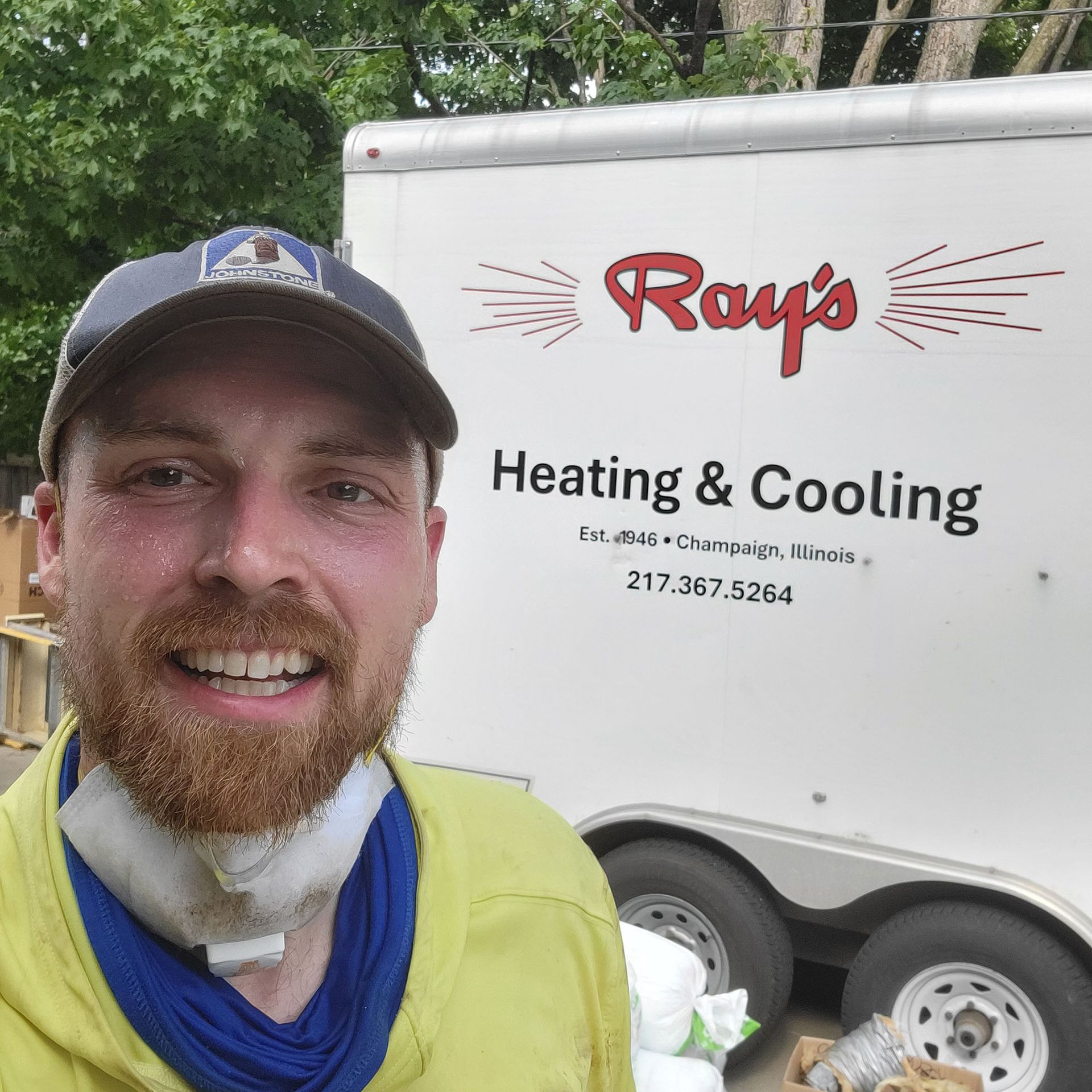 Smiling worker in a cap and safety vest in front of a Ray’s Heating & Cooling service truck.