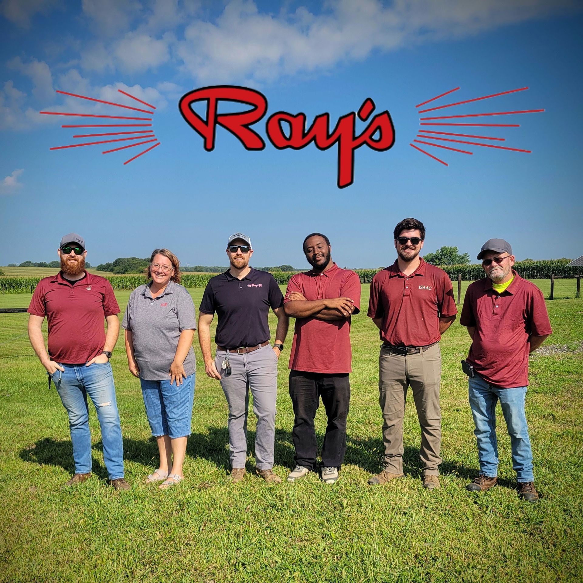 Six people standing on a grassy field under a blue sky with a red