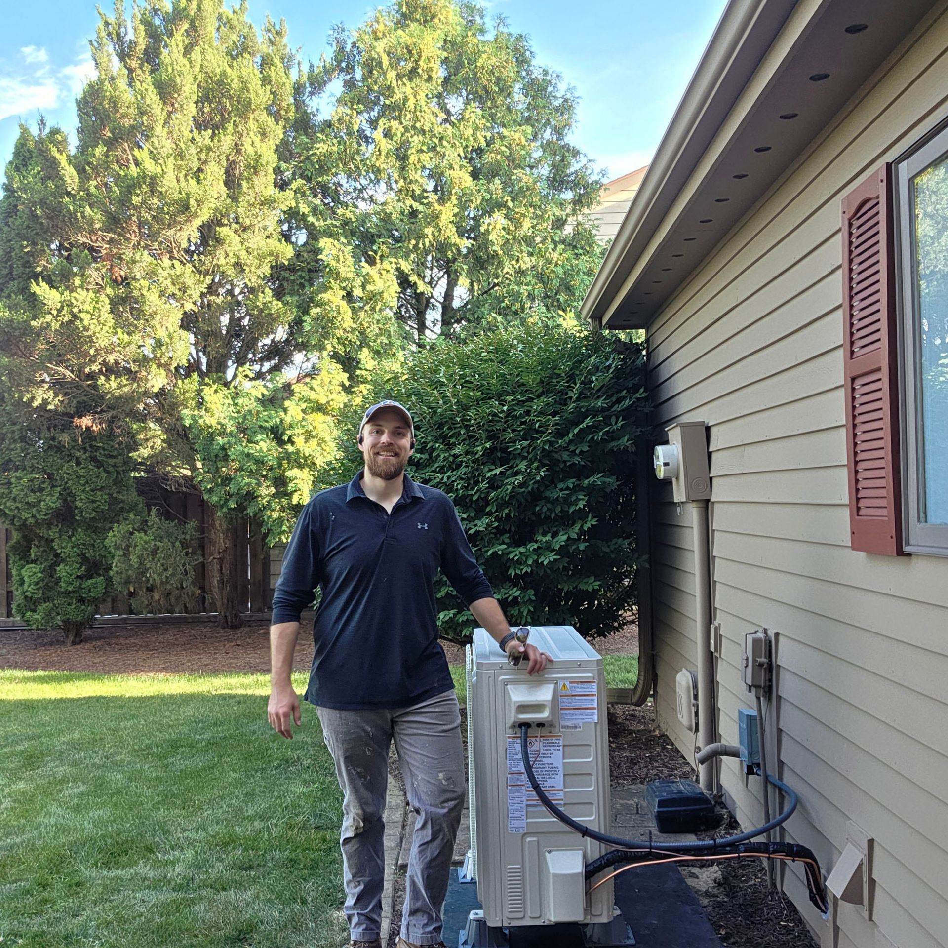 Technician standing beside outdoor HVAC unit next to a house, holding a tool outdoors.