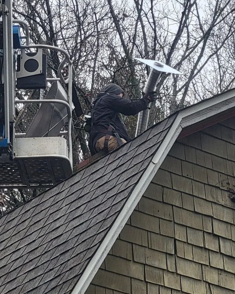 Worker on a lift using a shovel to clear snow from a steep house roof.