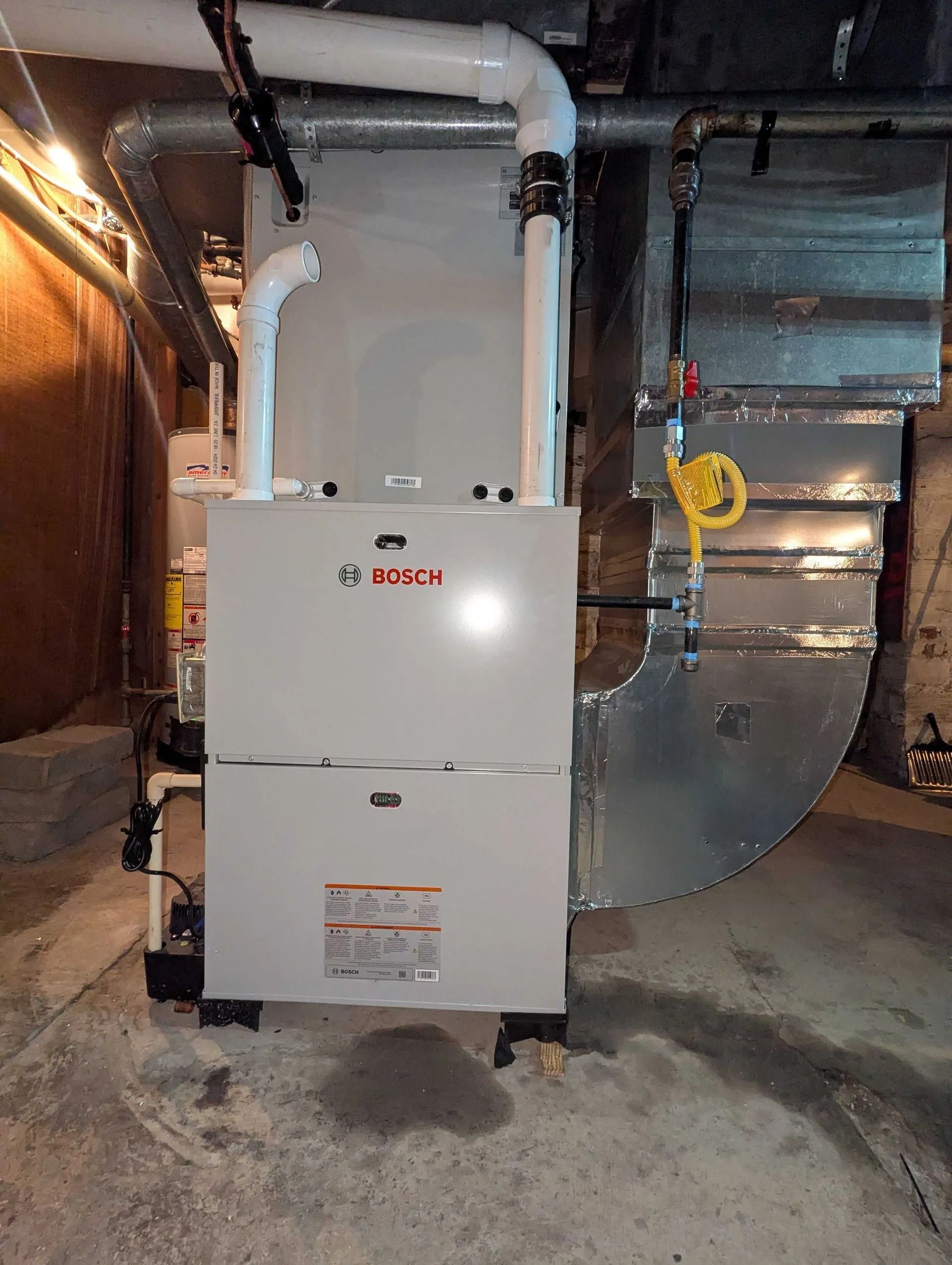 Basement furnace with white ductwork and a yellow gas shutoff valve against insulated walls