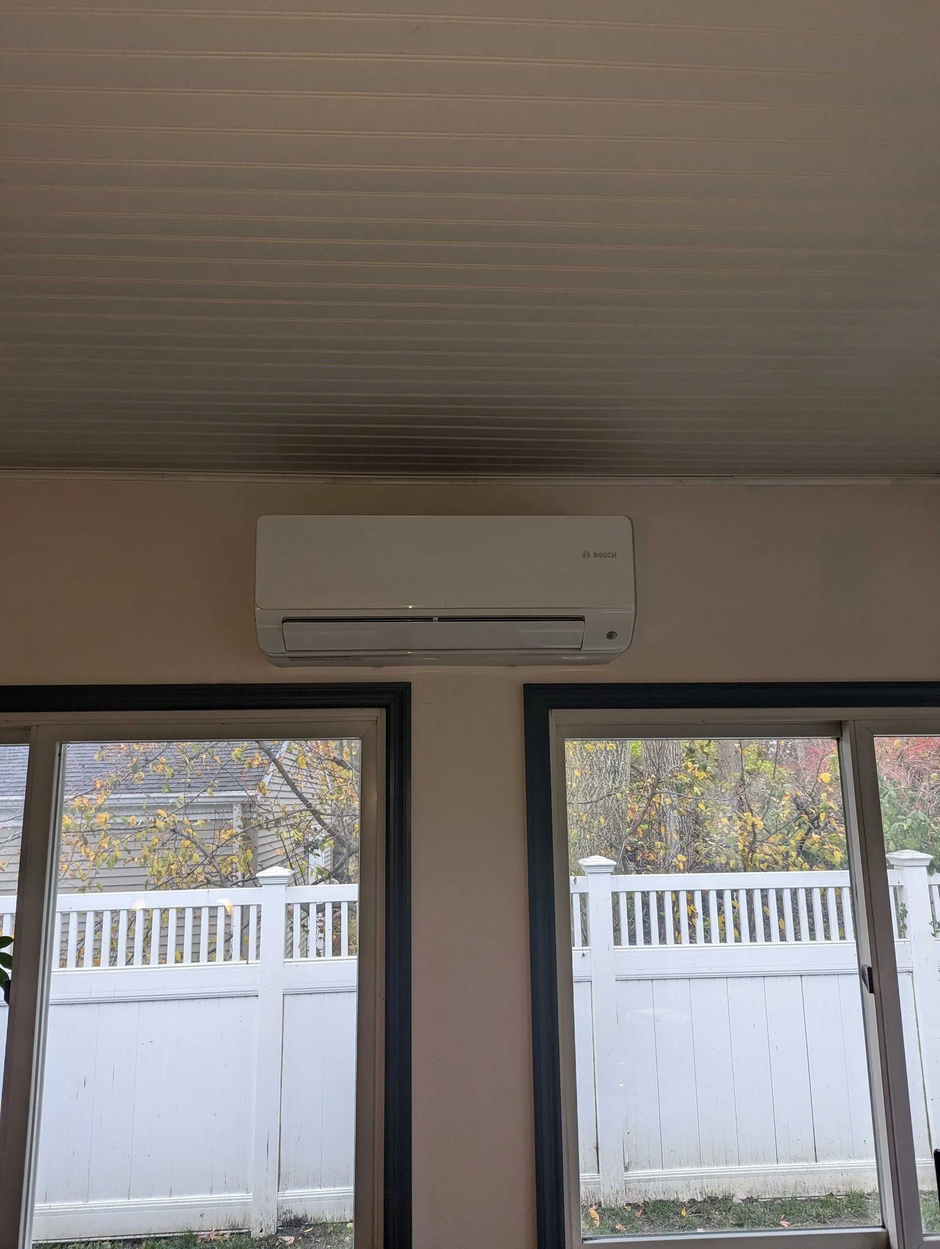 Wall-mounted air conditioner above two windows overlooking a snowy fenced yard.