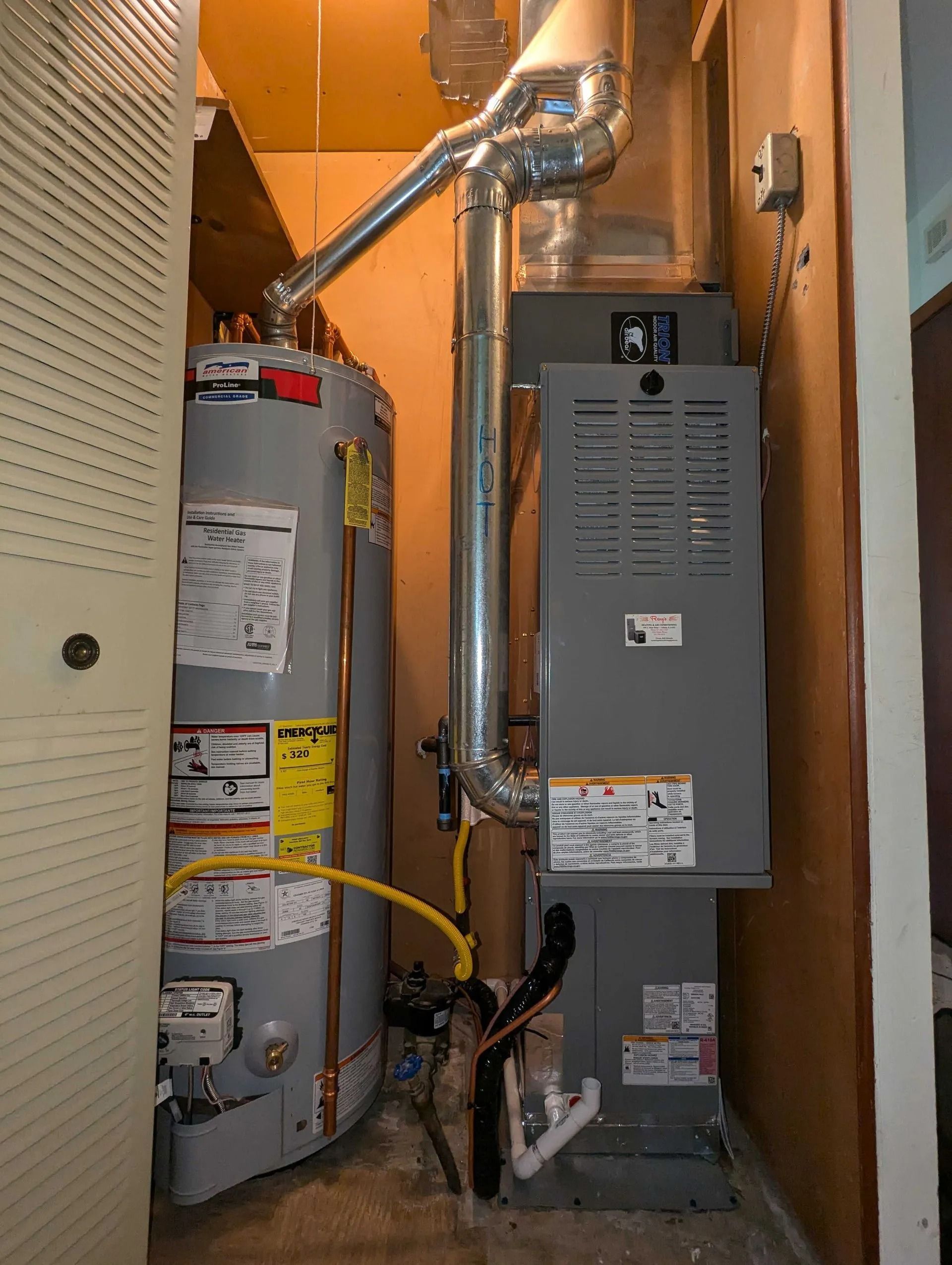 Narrow utility closet with a water heater, furnace, and exposed vent pipes against beige walls.