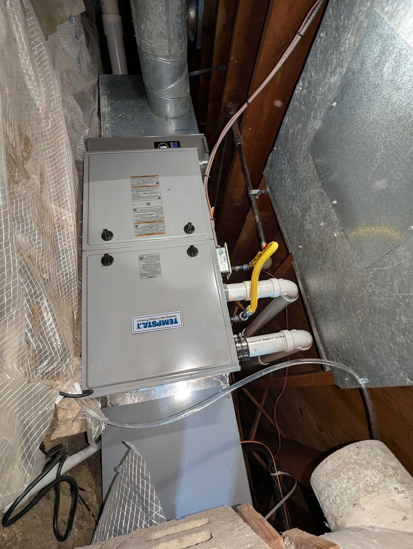 Attic HVAC furnace with silver ductwork and insulated walls, viewed in a cramped crawlspace