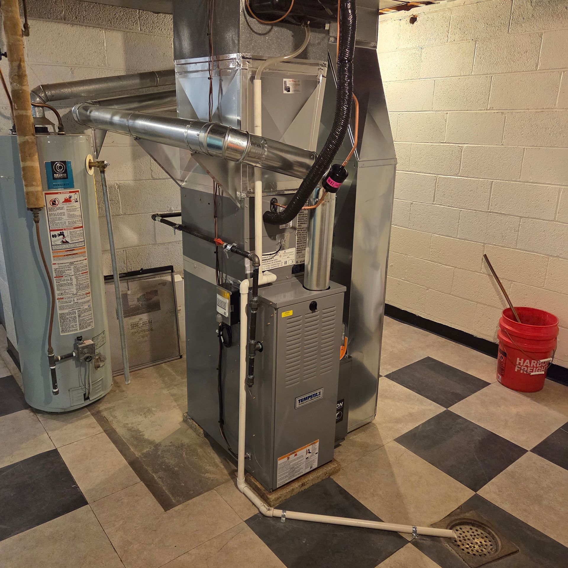 Basement furnace and water heater with ducts, pipes, and a floor drain in a utility room